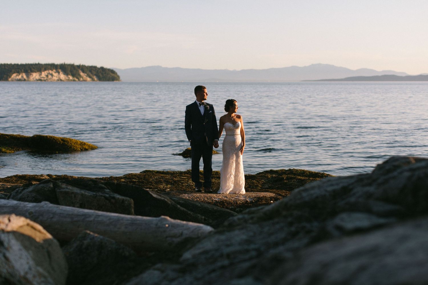 Couple standing on rocky coastline at sunset.