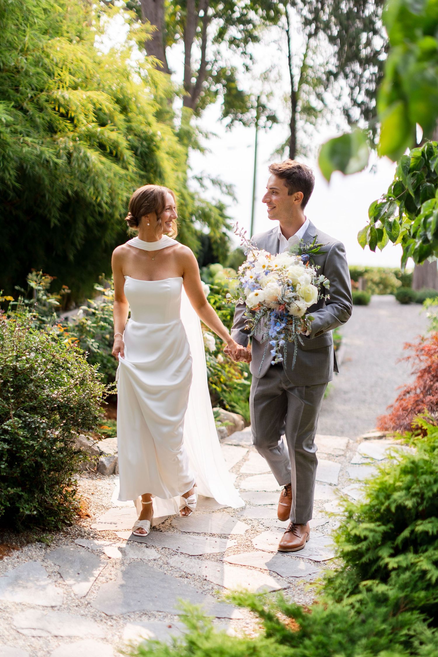 Bride and groom walking hand in hand through lush garden ceremony space.
