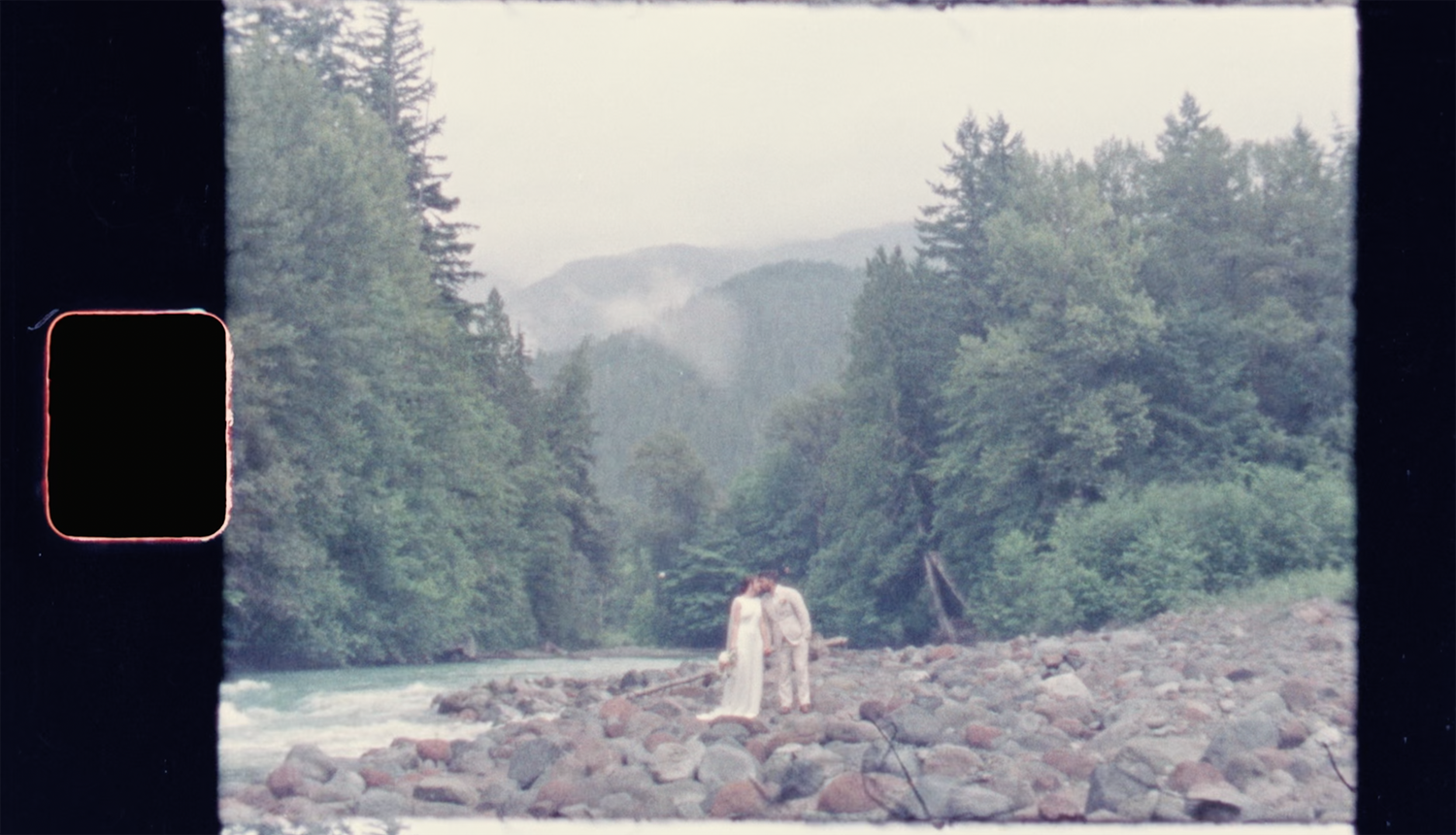 Super 8 wedding film frame of bride walking across rocky shoreline in British Columbia.
