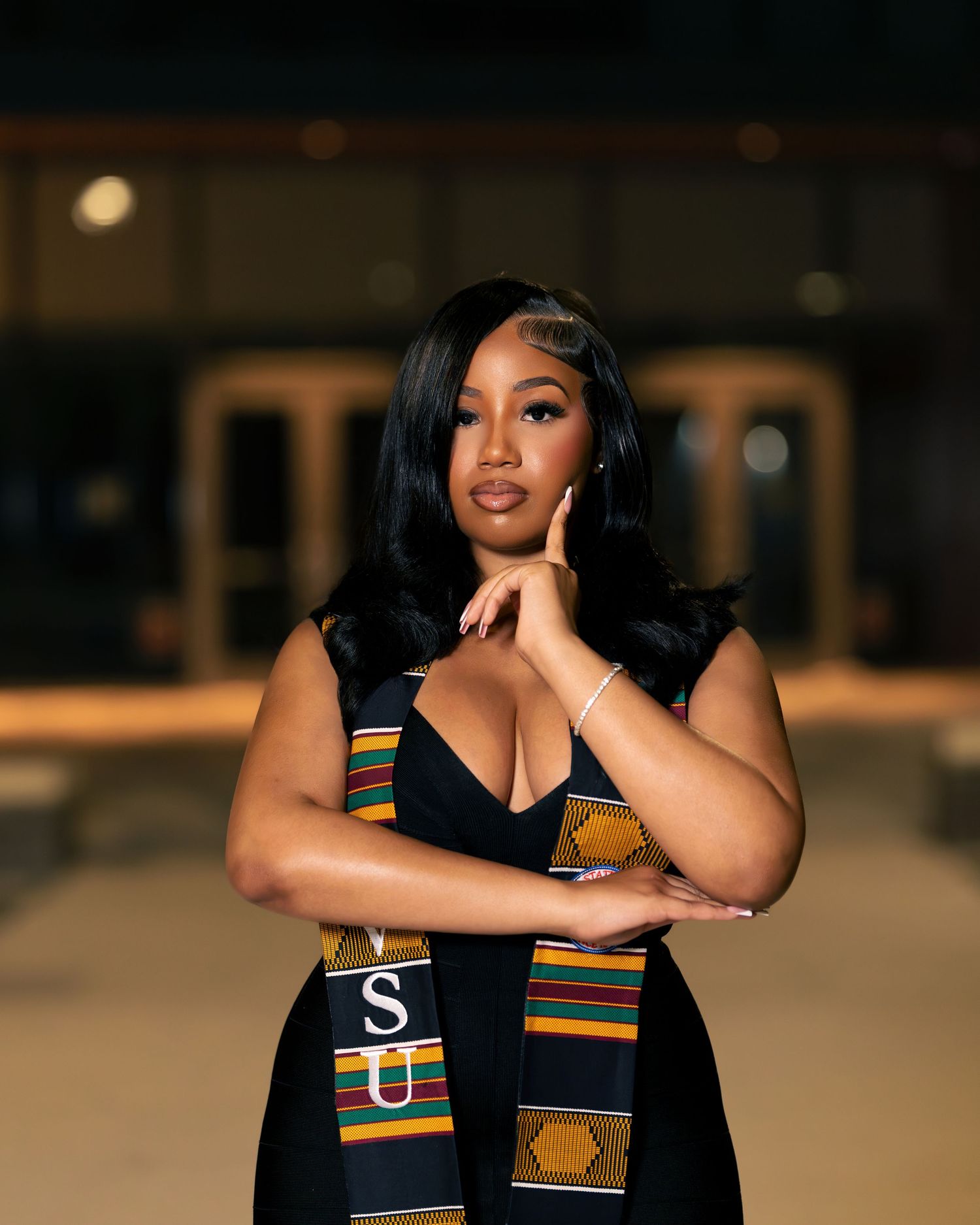 Young woman in black dress wearing a kente cloth graduation stole, posing confidently at a VSU graduation ceremony.