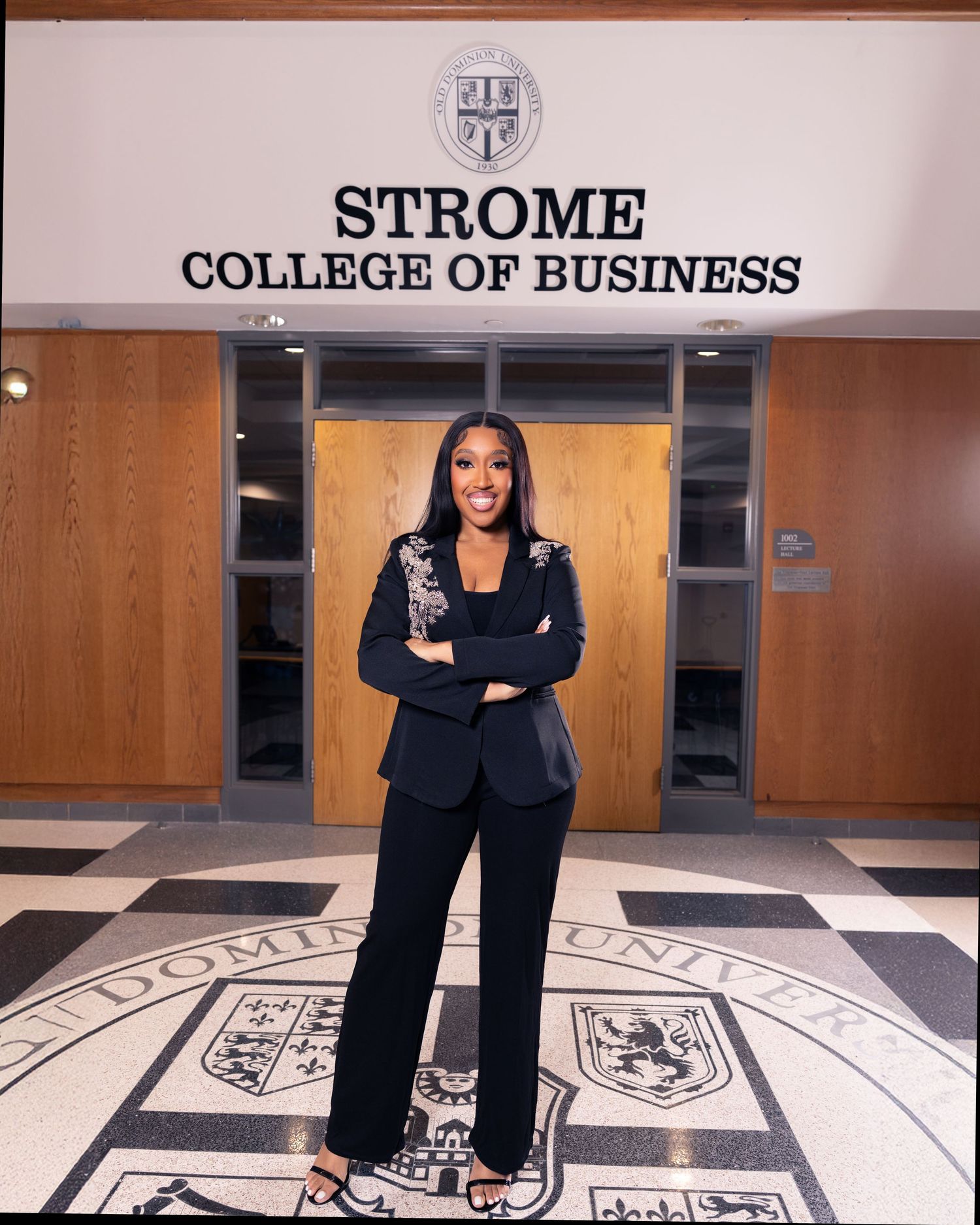 Woman in black suit standing confidently at Strome College of Business entrance at Old Dominion University.