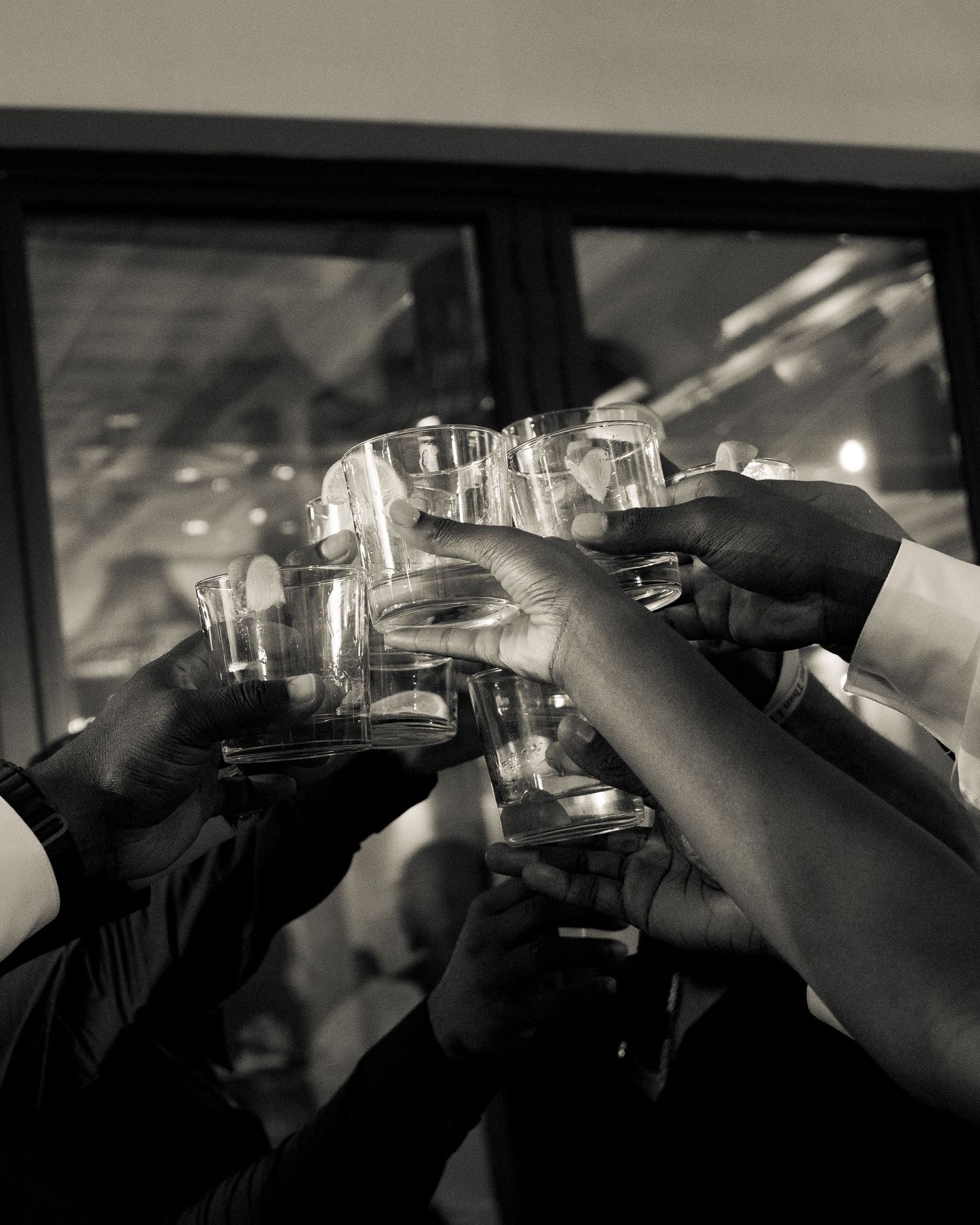 Black and white photo of diverse hands raising glasses in a celebratory toast at a formal event.