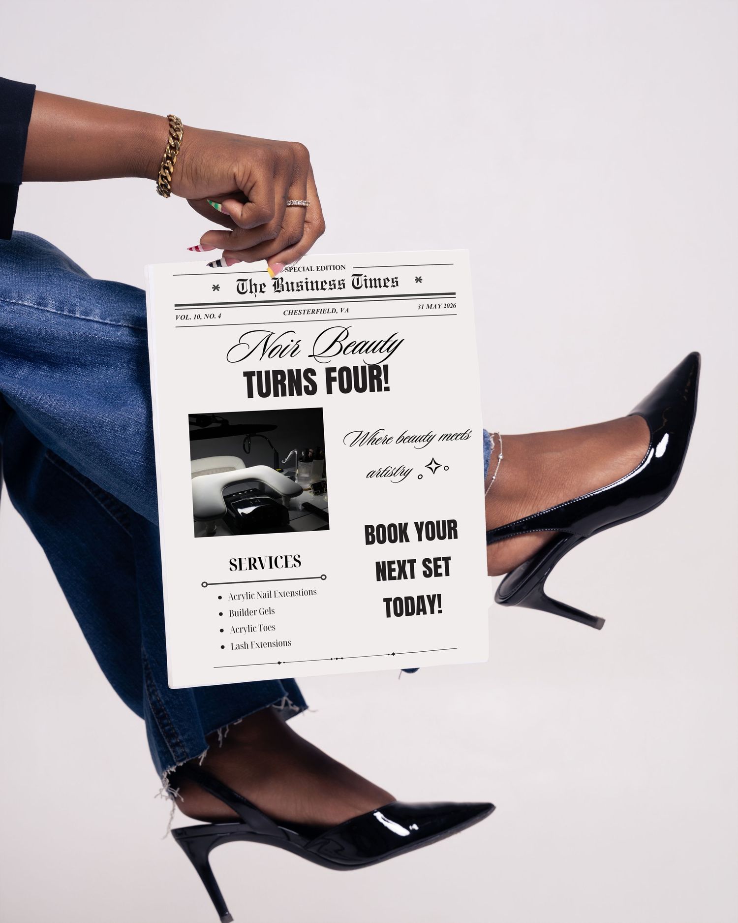 A person holds a newspaper-style flyer for Noir Beauty's fourth anniversary, wearing black heels and denim jeans.