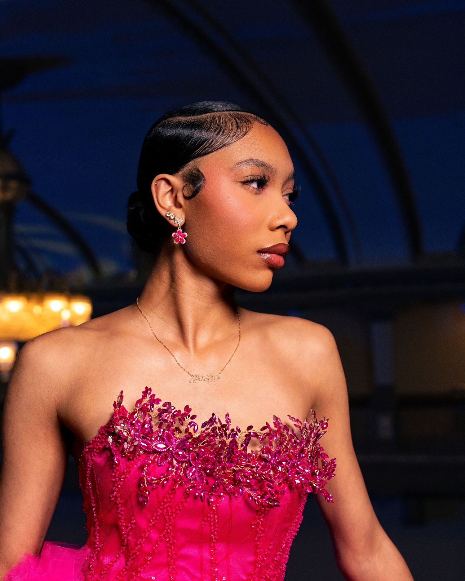 Young woman in a strapless hot pink beaded gown with floral embellishments, wearing pink earrings and a delicate necklace.