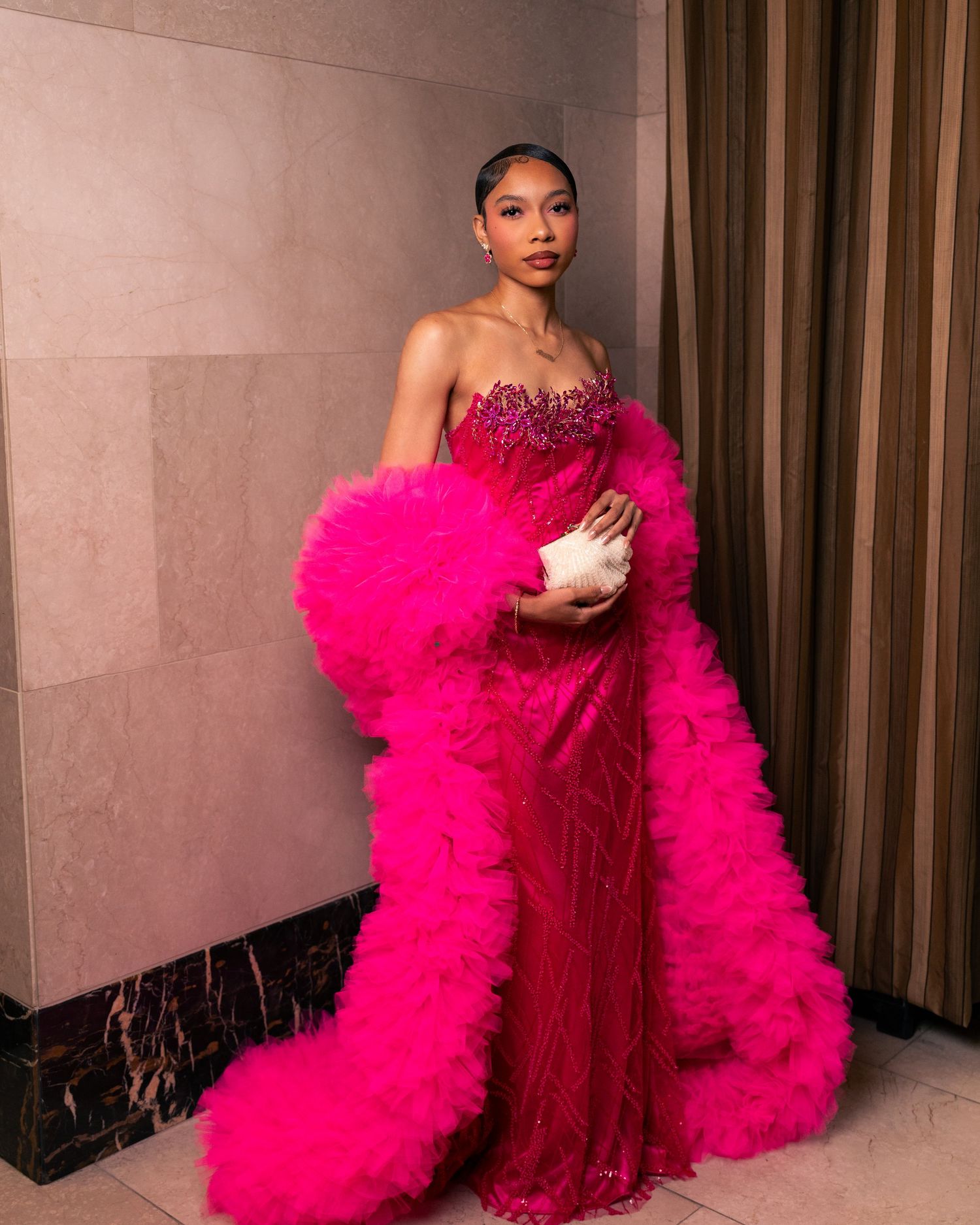 Woman in a stunning hot pink strapless tulle gown with feather trim and beaded bodice, holding a white clutch.