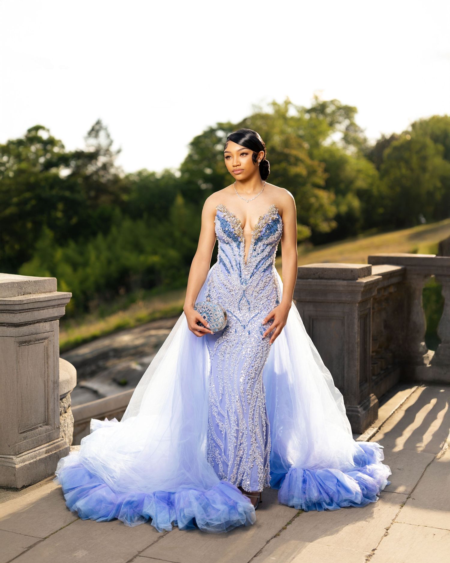 Woman in a stunning blue sequined mermaid prom gown with tulle overskirt on an outdoor stone terrace.