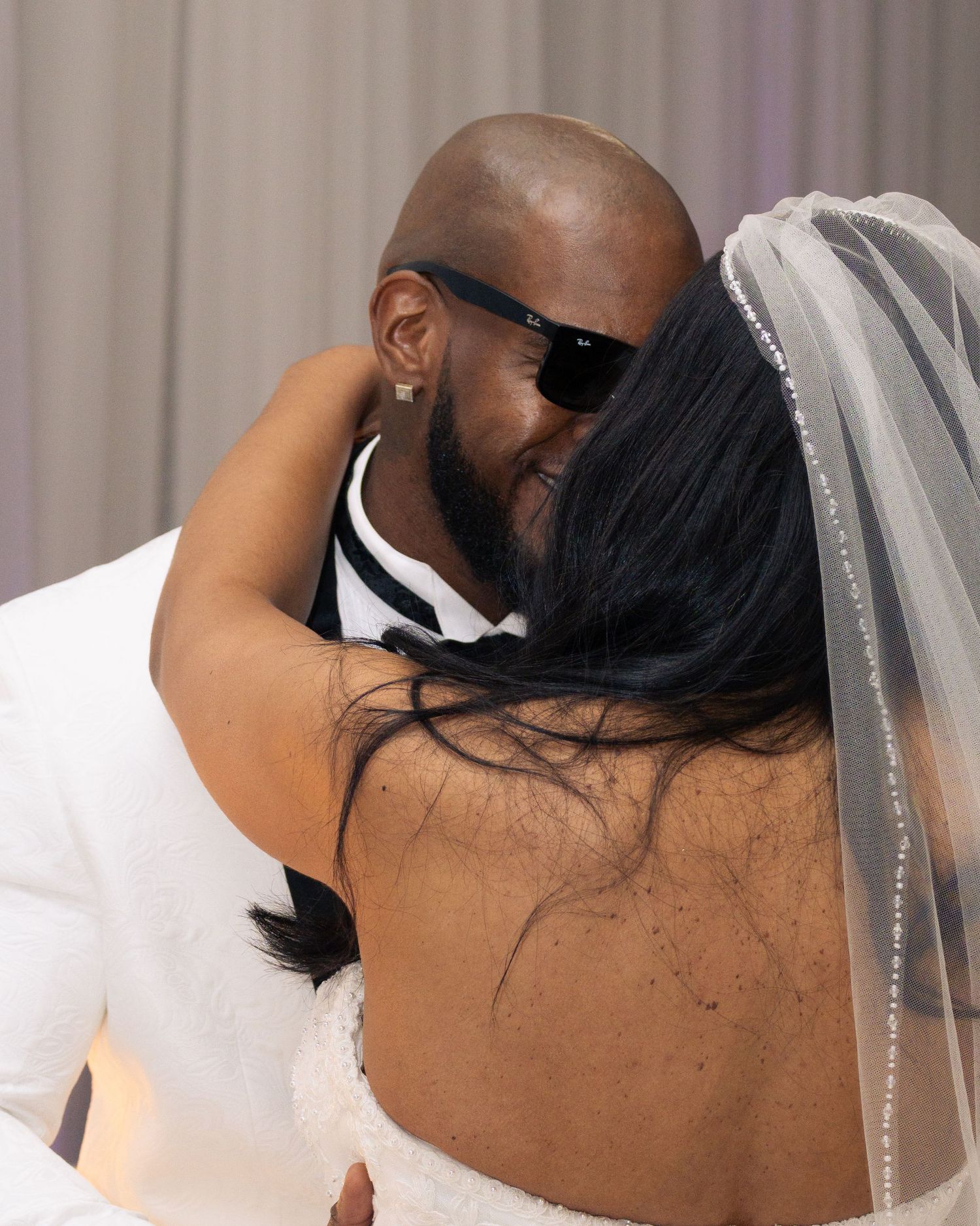A couple shares an intimate embrace during their wedding ceremony, the bride wearing a veil and backless gown.