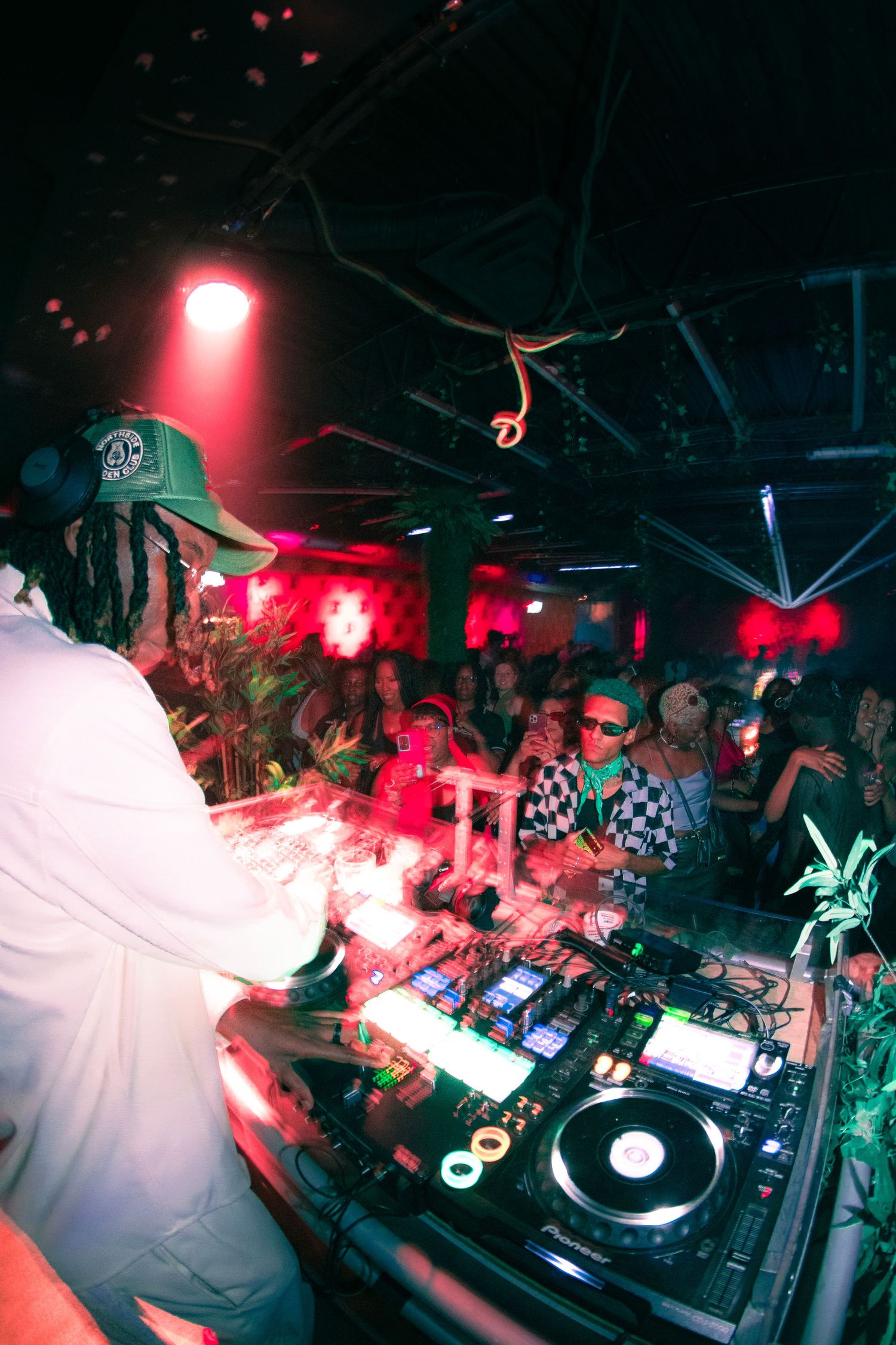 DJ performing at a nightclub with turntables under dramatic red lighting and smoke effects.