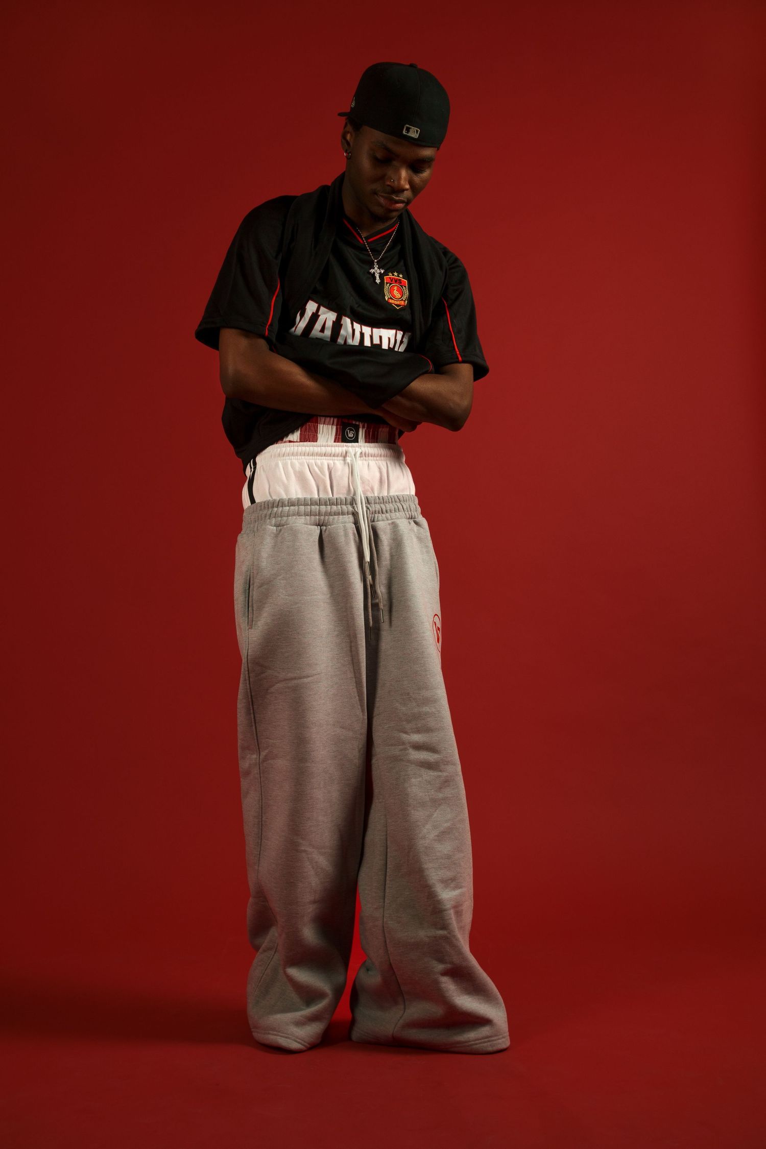 Urban style poses in oversized gray sweatpants against red background.