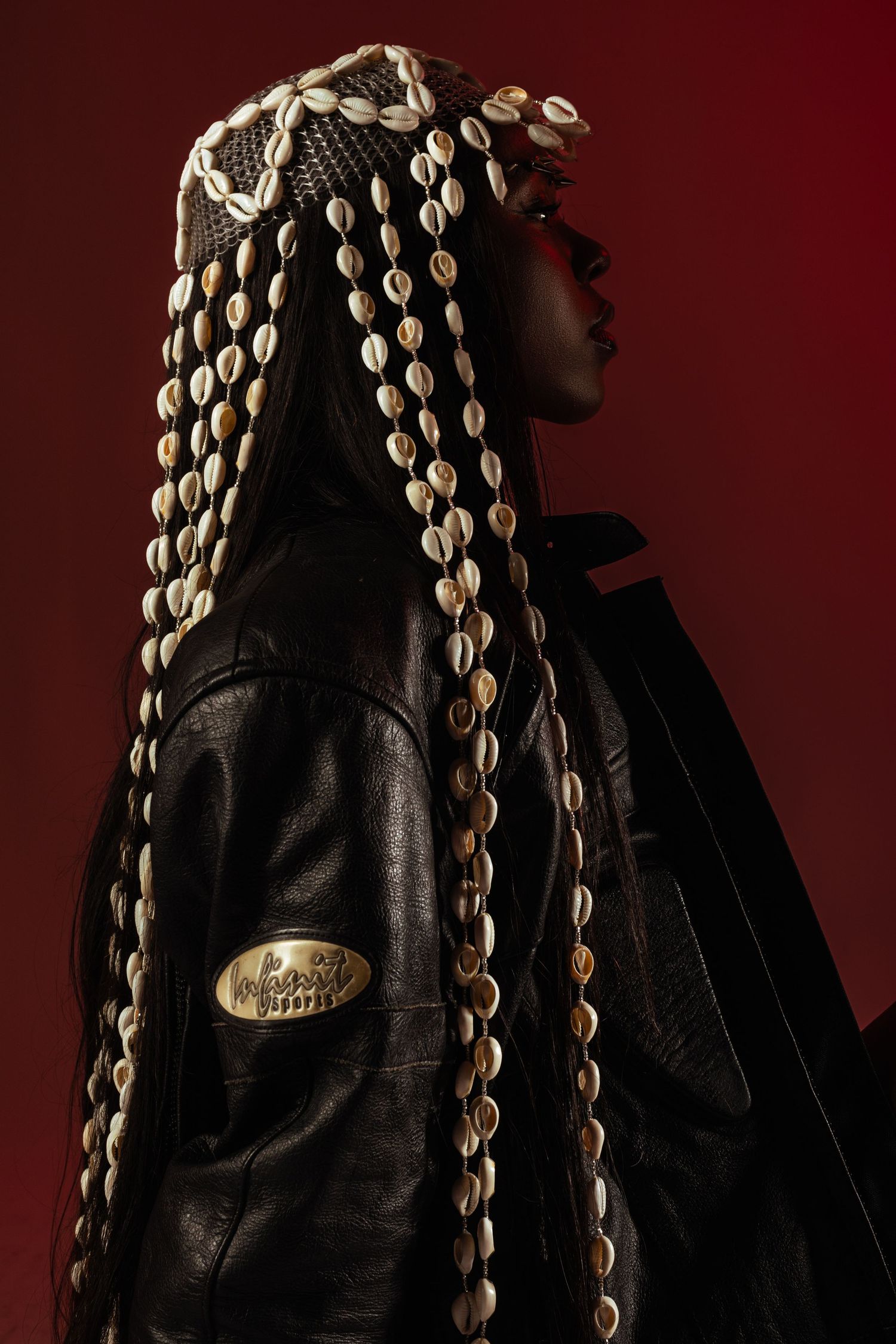 Stylized portrait with decorative shell accessories against deep red background.