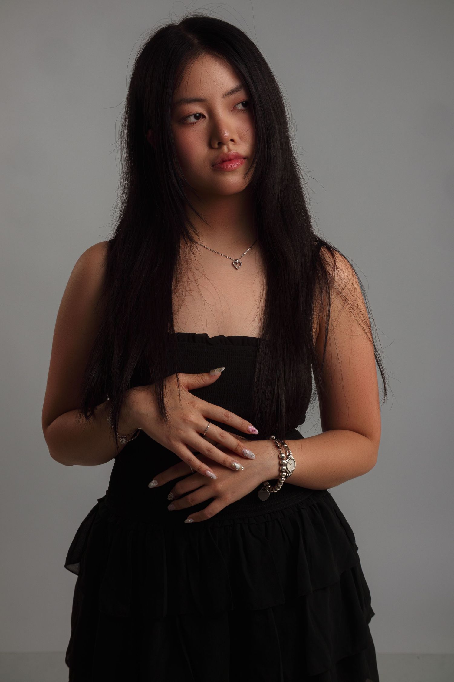 Studio portrait with dramatic lighting and black dress against grey background.