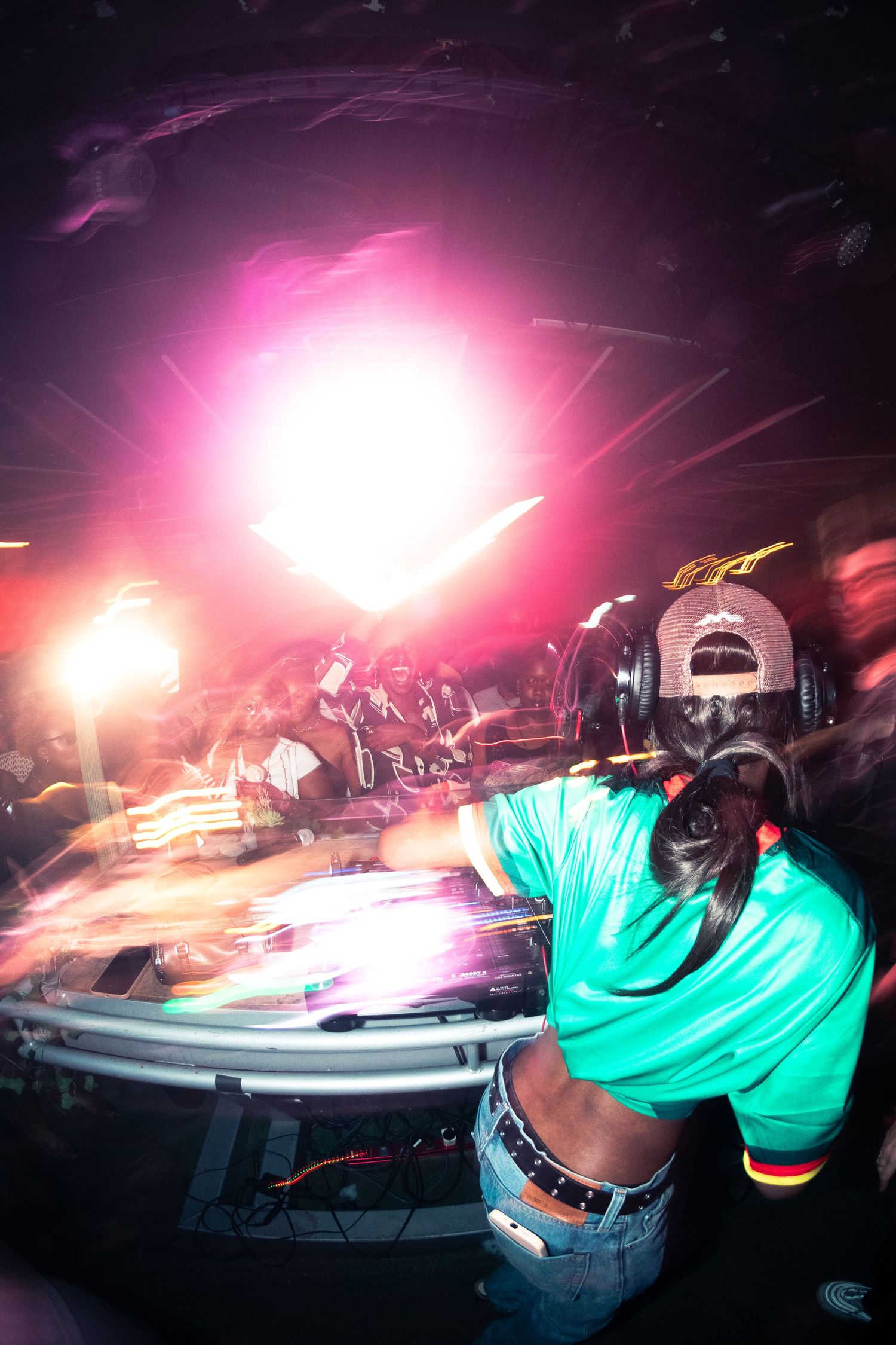 DJ mixing music on turntables under bright pink stage lights at a nightclub.