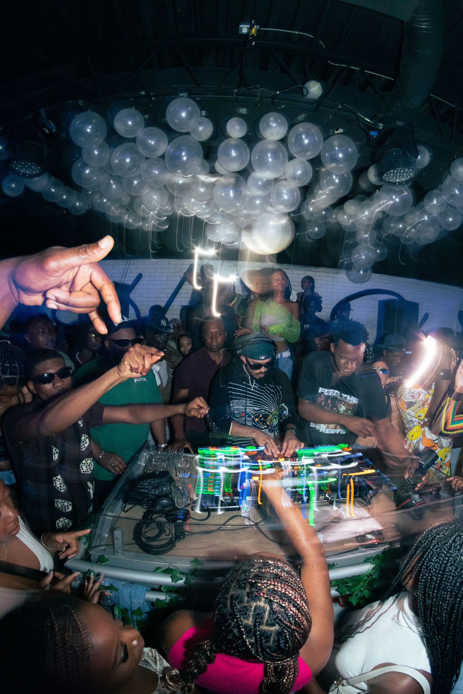 Crowded dance floor under white balloon decorations with DJ equipment in the foreground.