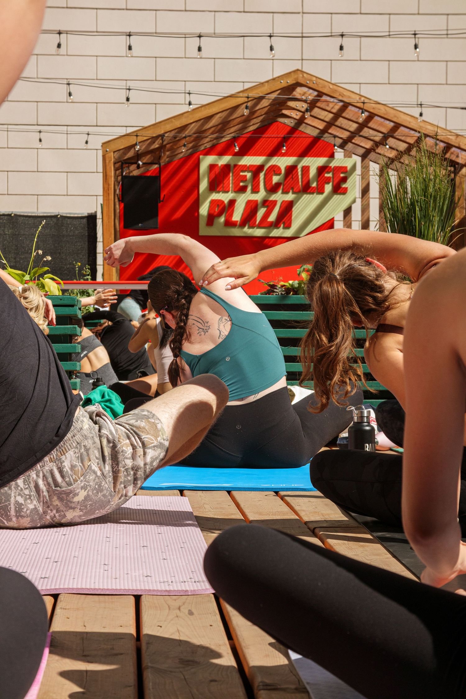 Group doing outdoor yoga exercises in front of brick wall with red signage.