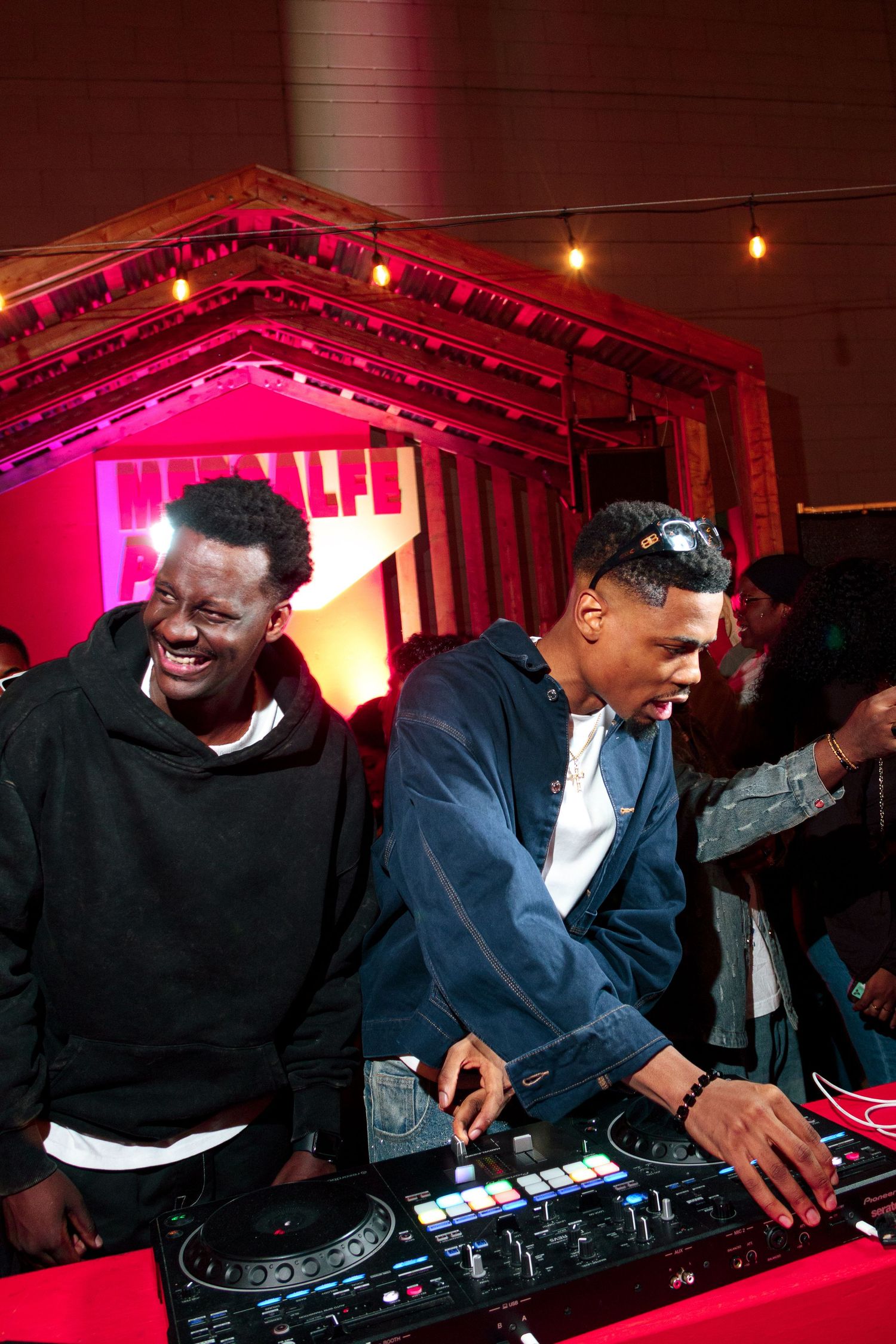 DJs performing at a music event with pink neon lighting in the background.