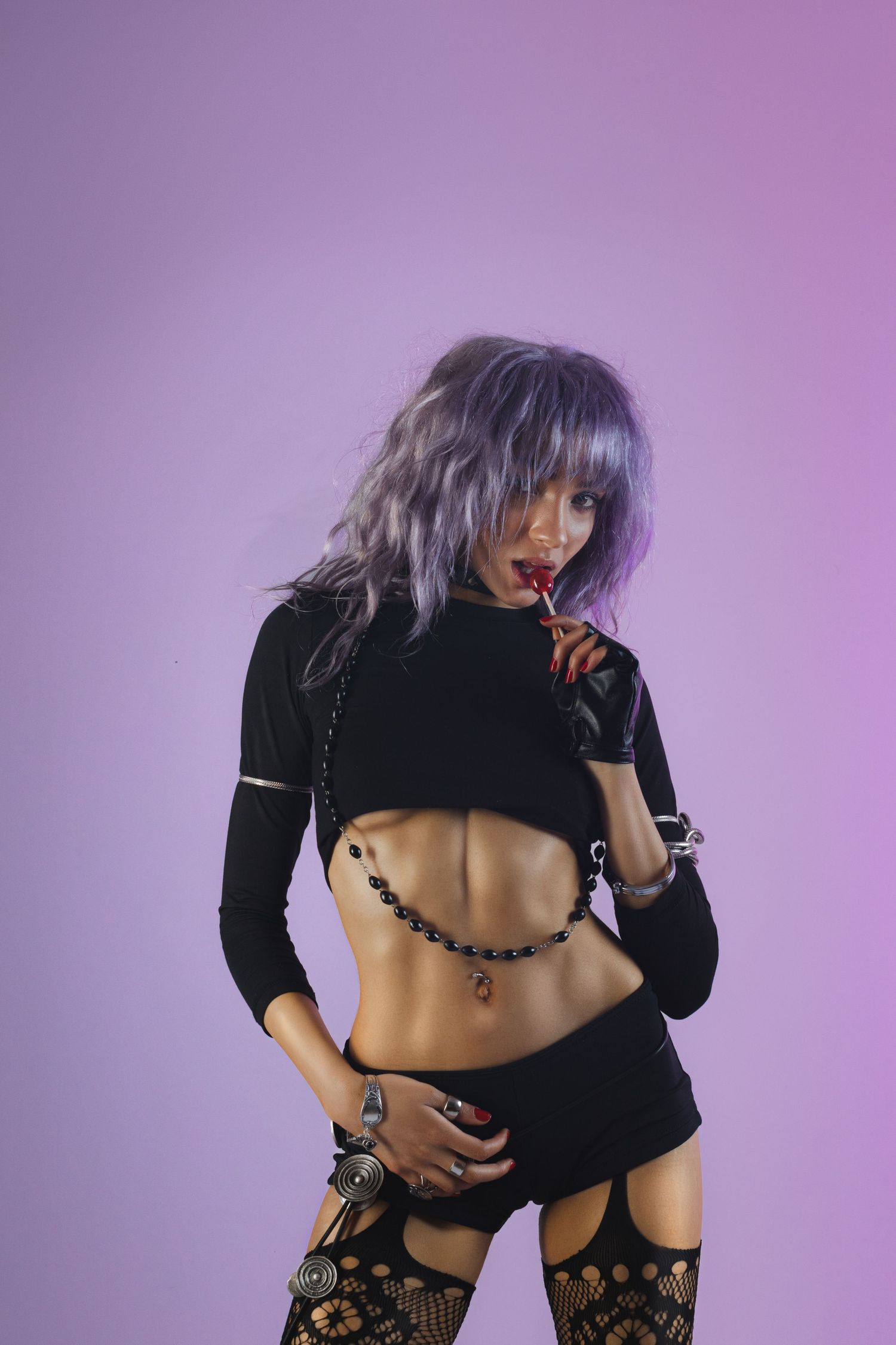 Fashion model in black crop top and fishnet stockings poses on purple background.