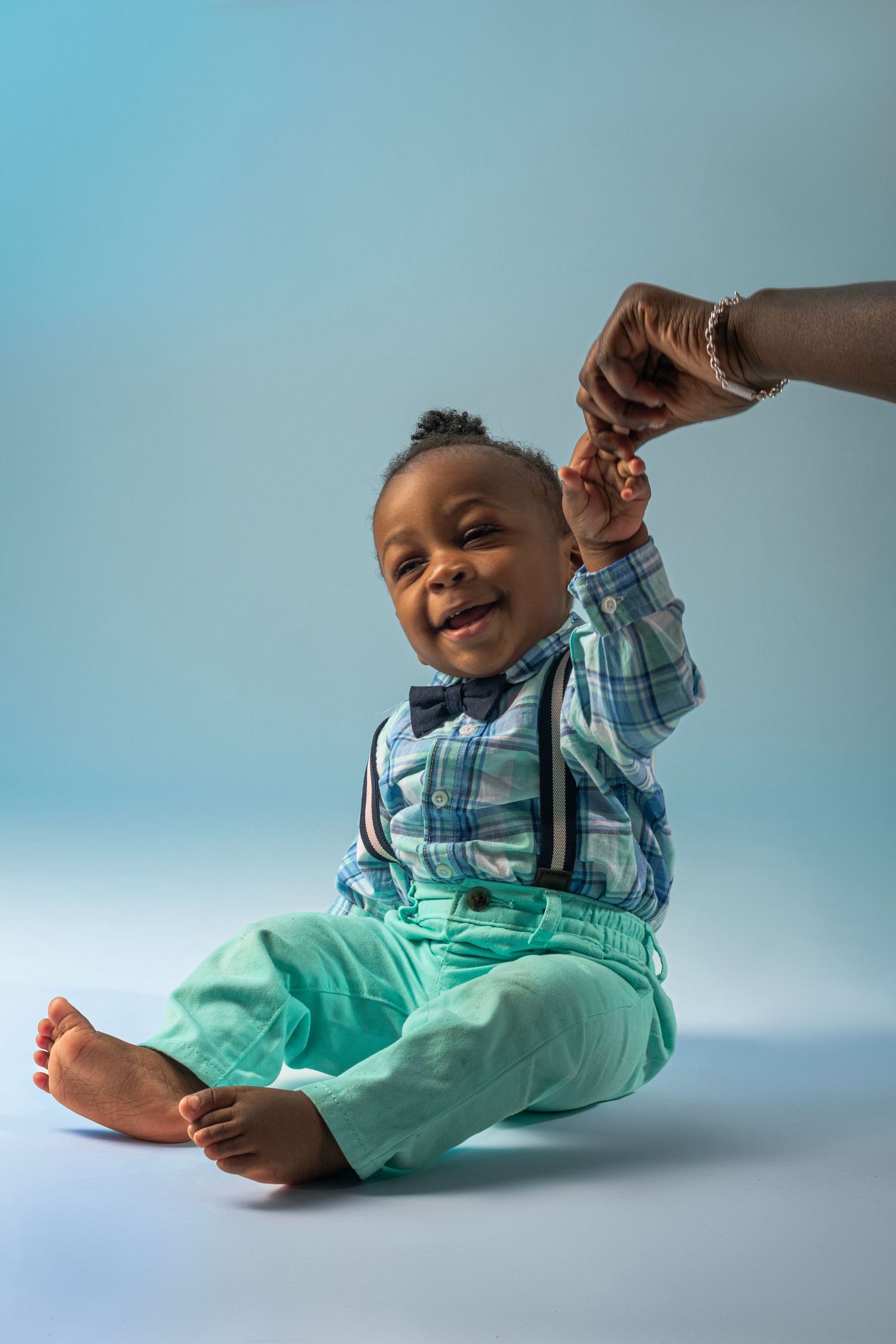 Baby in plaid shirt and mint pants lying on blue background showing playful expressions.