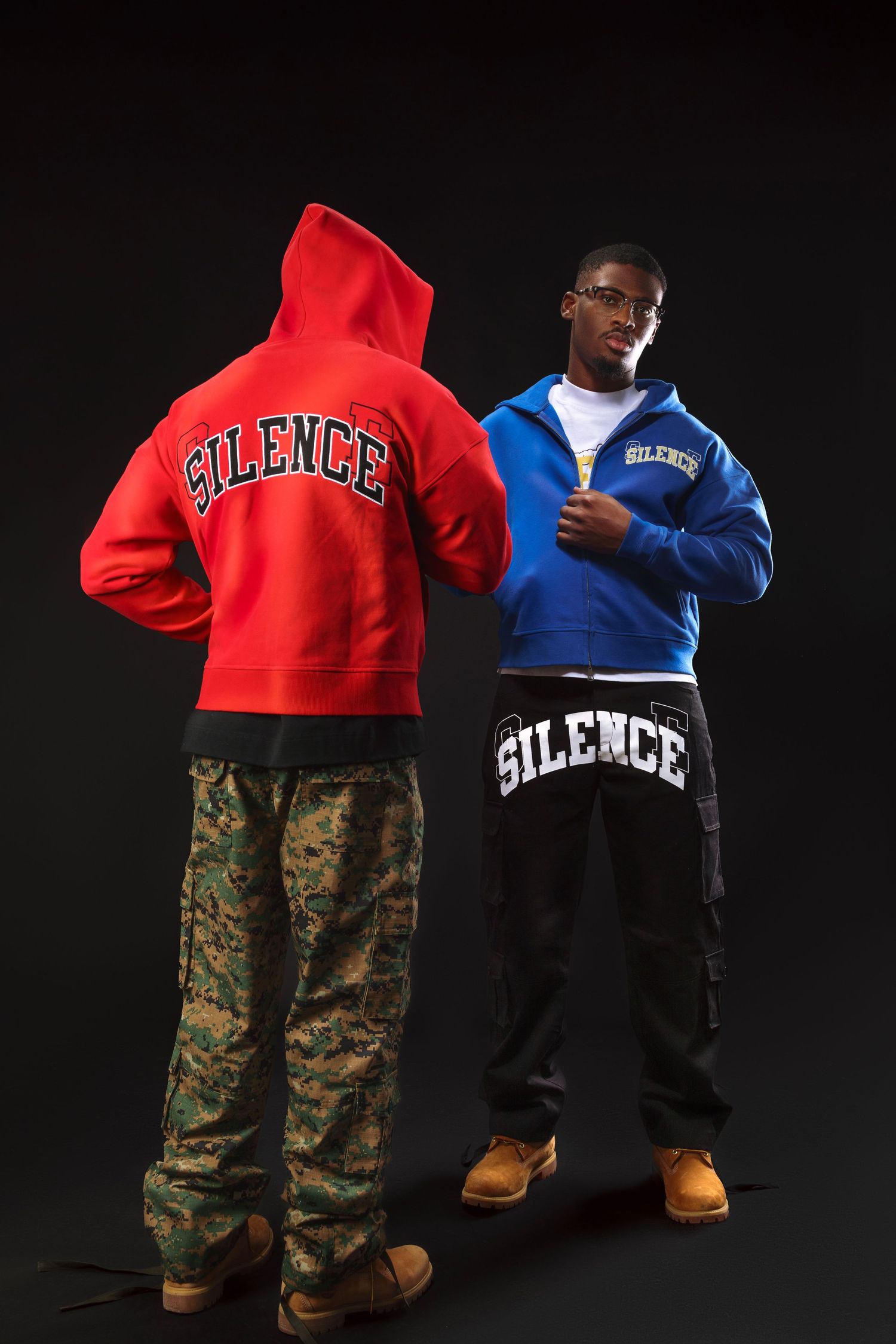 Two people modeling red and blue hoodies with 'Silence' text and camo pants against dark background.