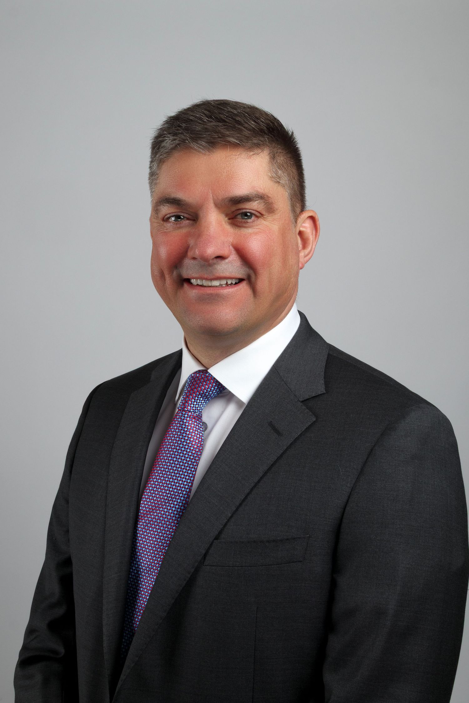 Professional headshots of person in dark suit with purple tie against grey background.