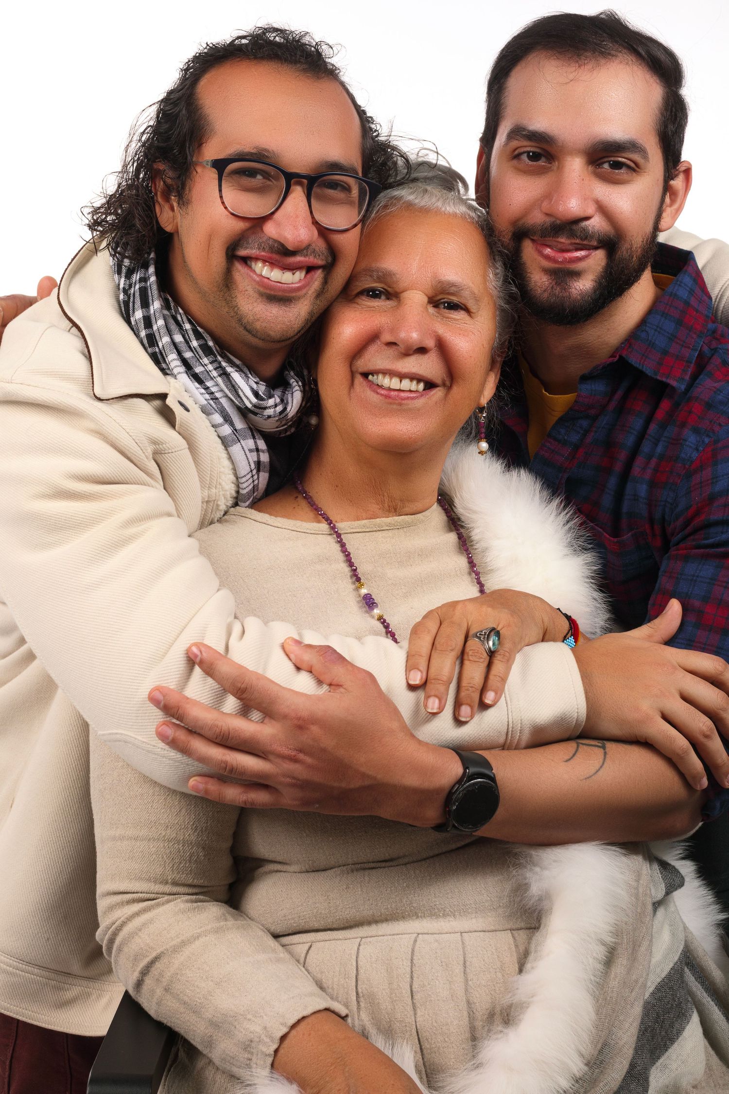 Three family members embrace warmly while posing together against white background.