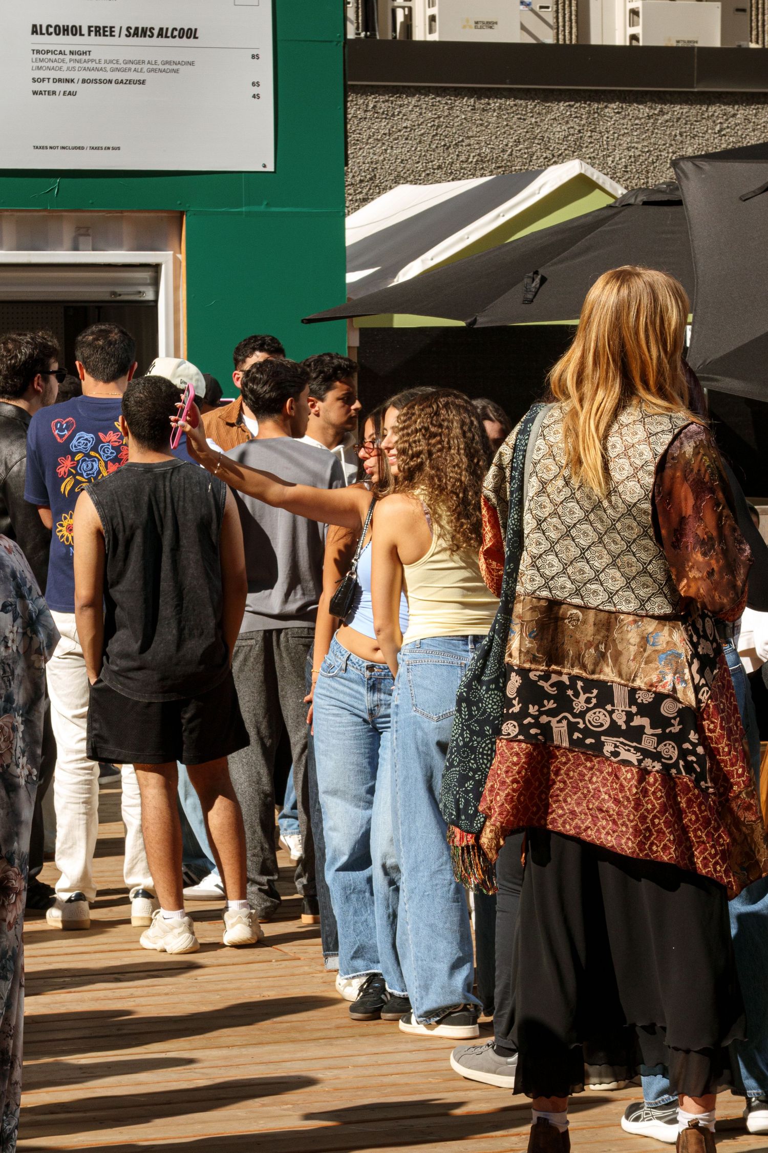 Crowd of people standing in line outside a building with green signs.