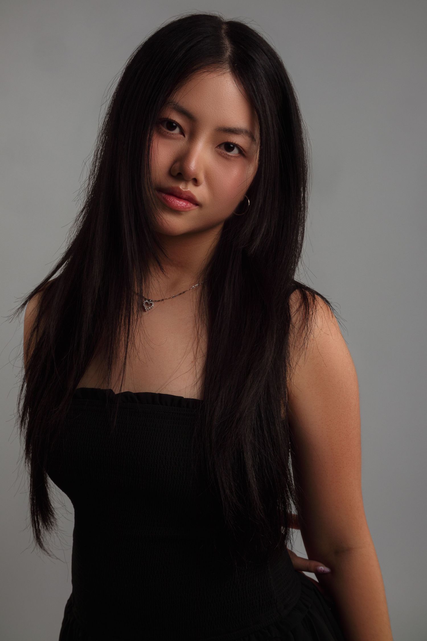 Studio portrait of woman with long black hair wearing black top against gray background.