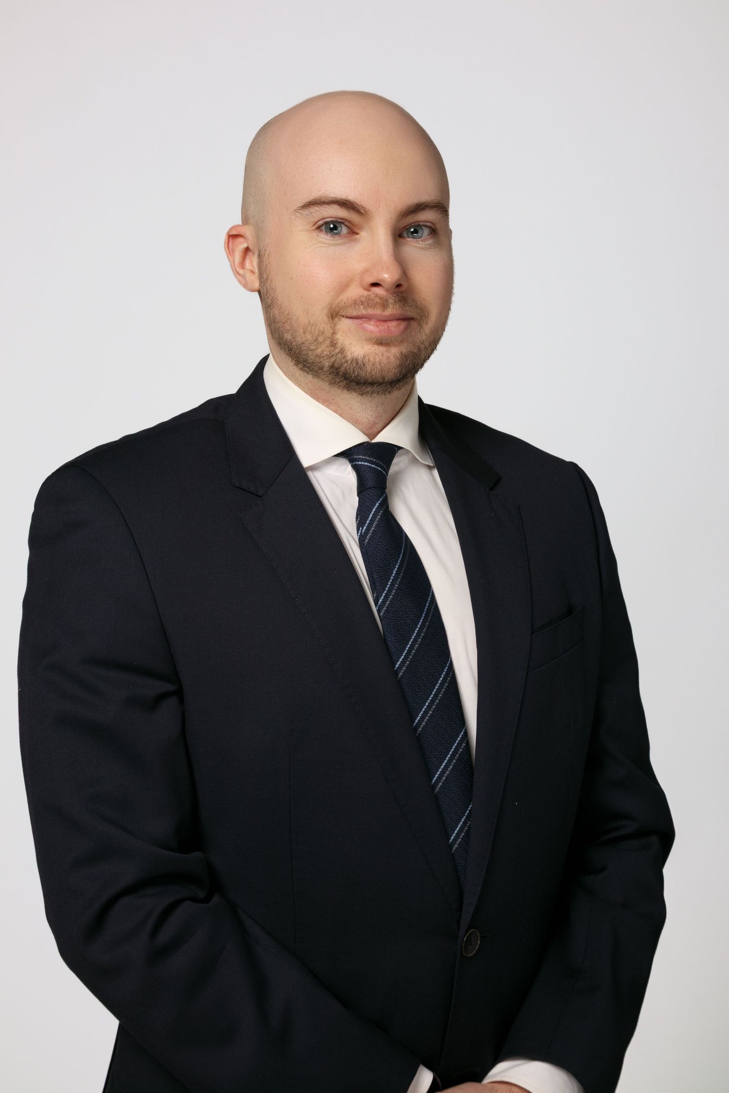 Professional headshot of a person in a black suit and striped tie against a light gray background.