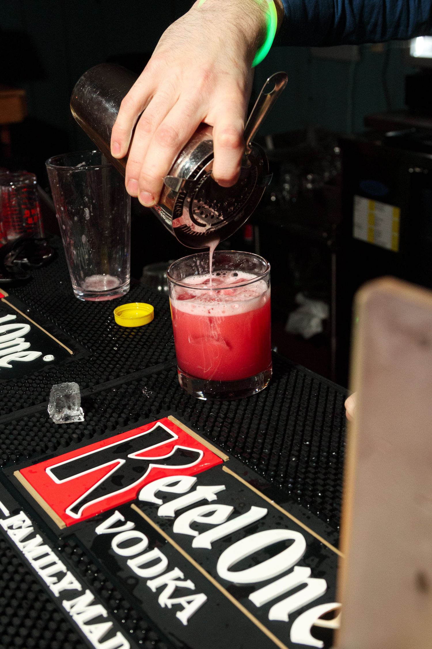 Bartender preparing red cocktails on a black bar mat.