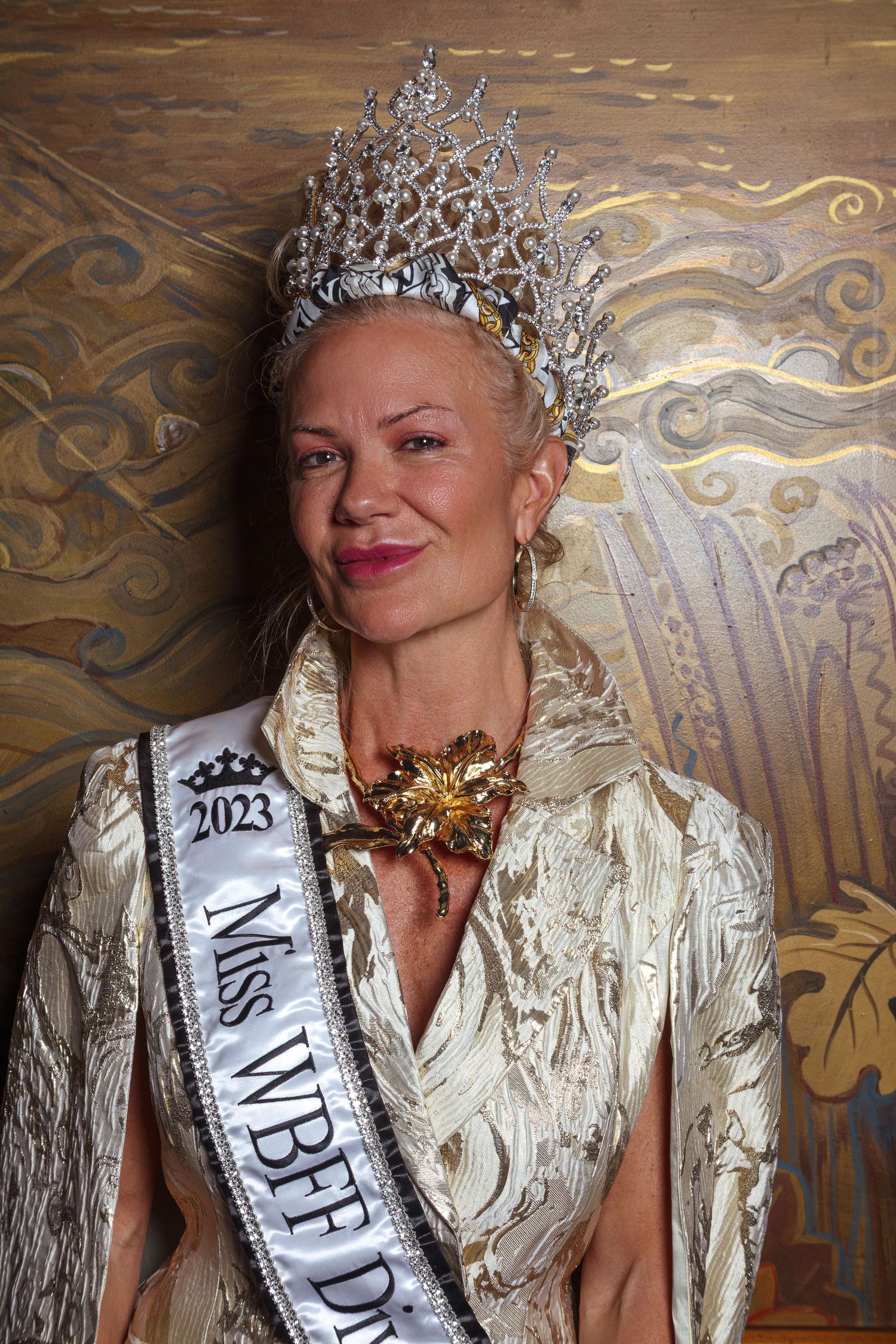 Woman wearing 2023 Miss WBFF crown and sash in gold jacket poses for portrait photo.