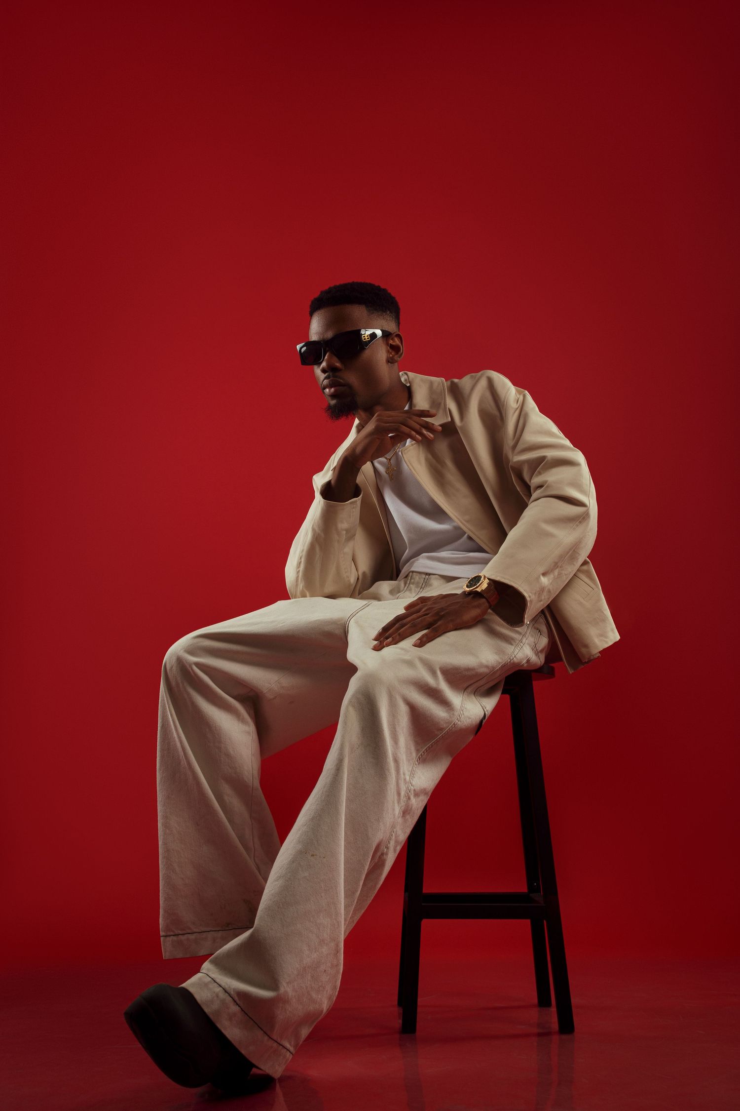 Figure in beige outfit posing dramatically against red backdrop.