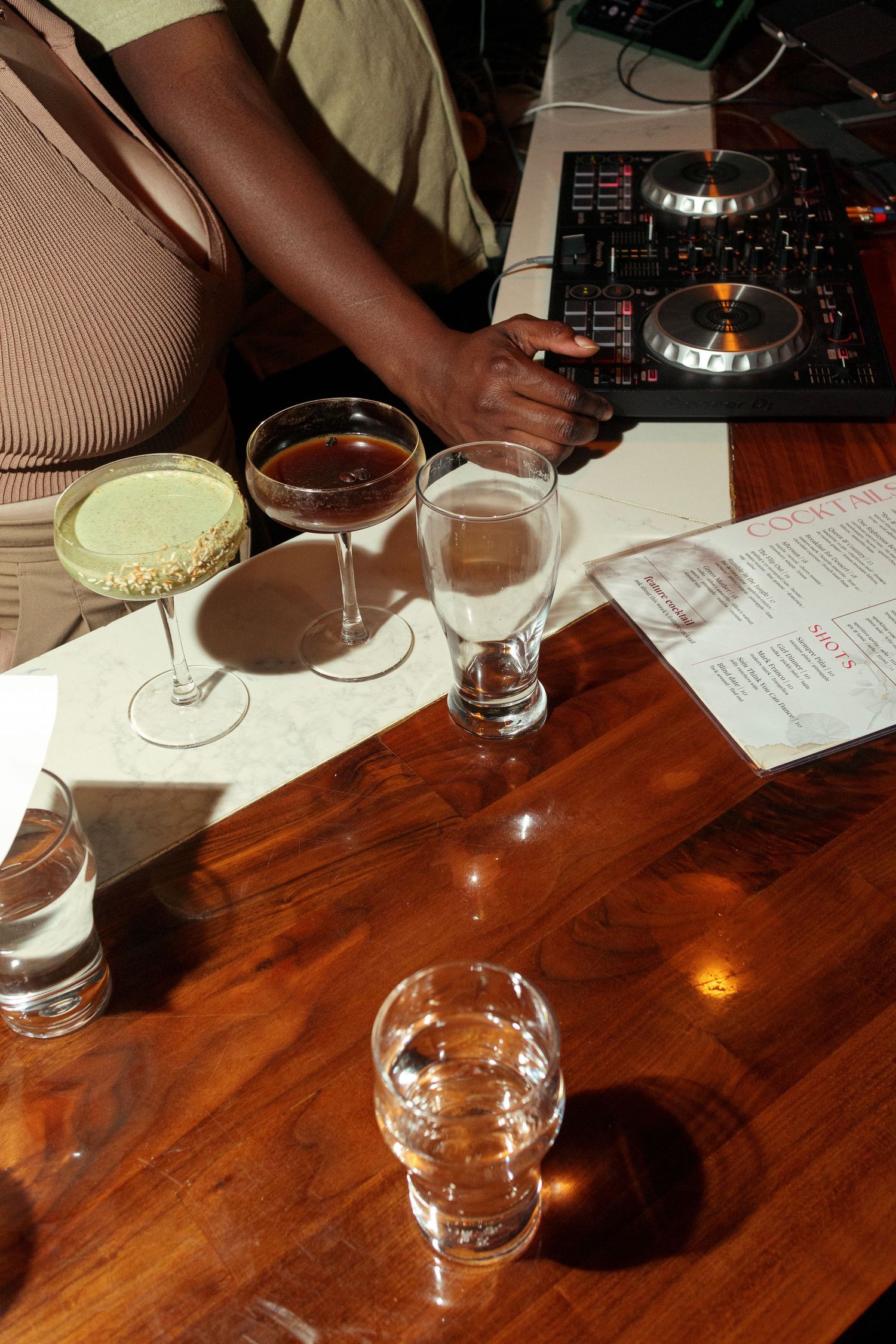 Empty cocktail glasses sit on a wooden bar table with menus.