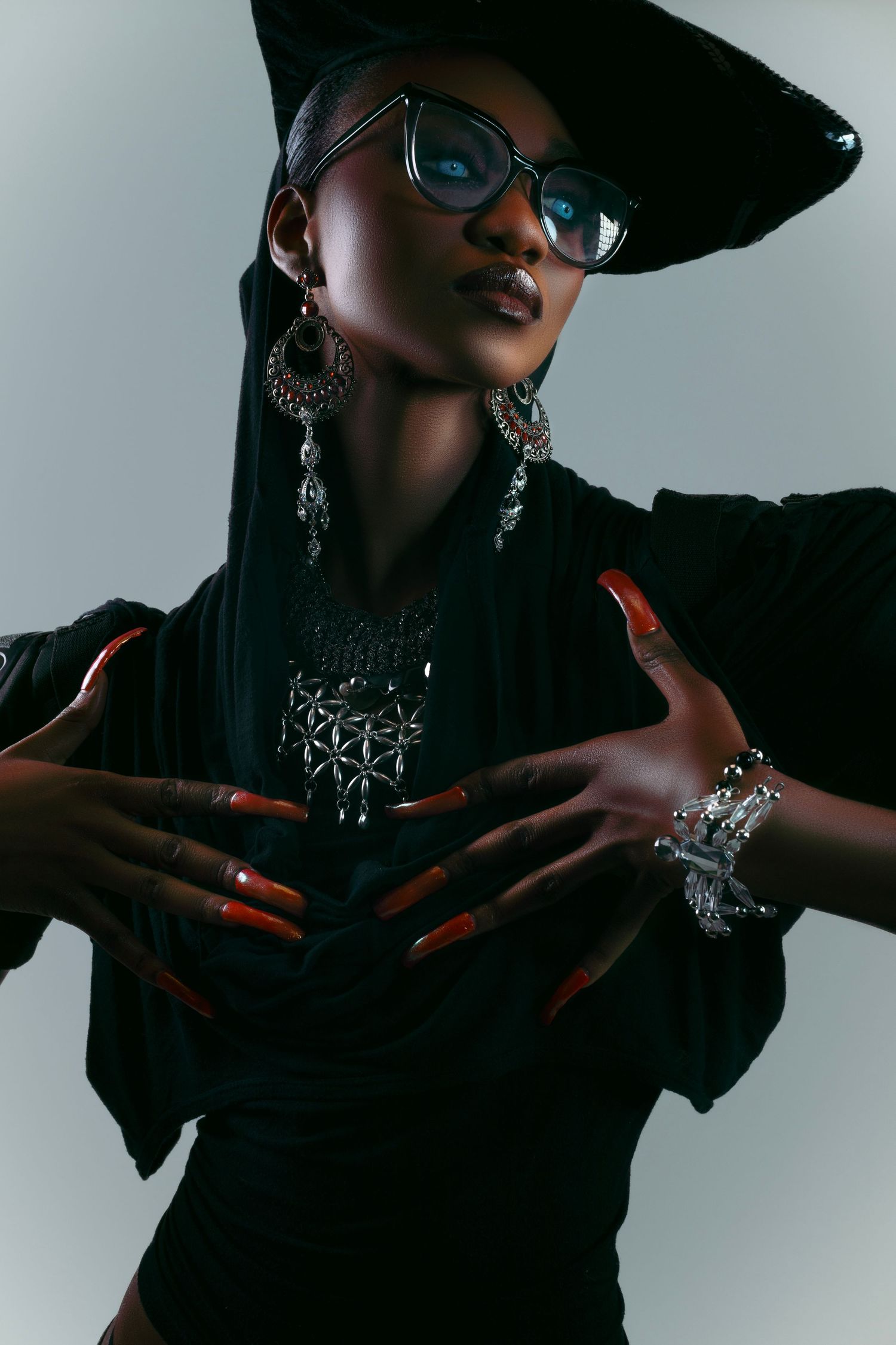 Stylish fashion shoot with dramatic lighting showing jewelry and hand gestures against gray background.