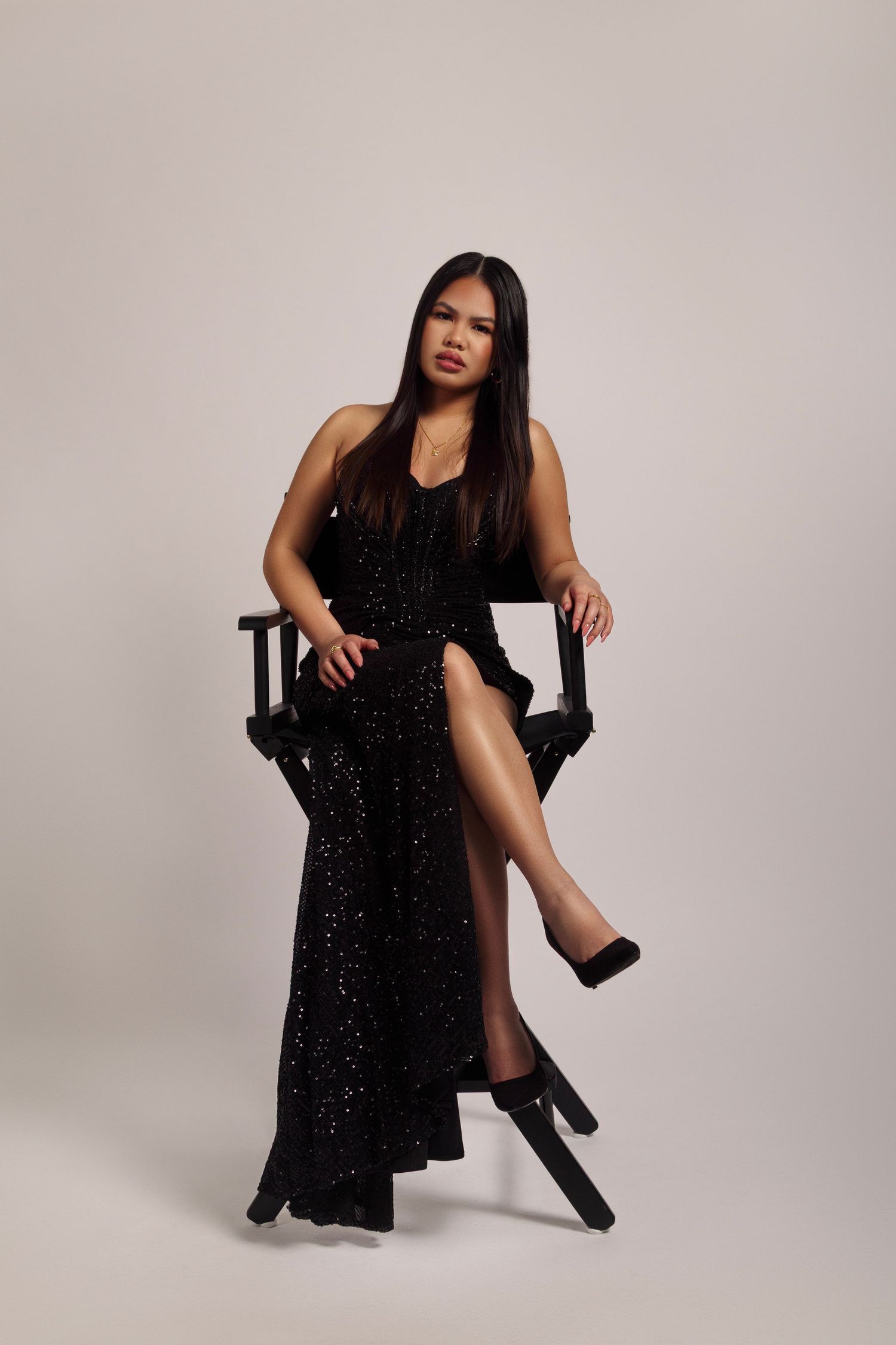 Woman in sparkling black evening gown sitting elegantly in director's chair.