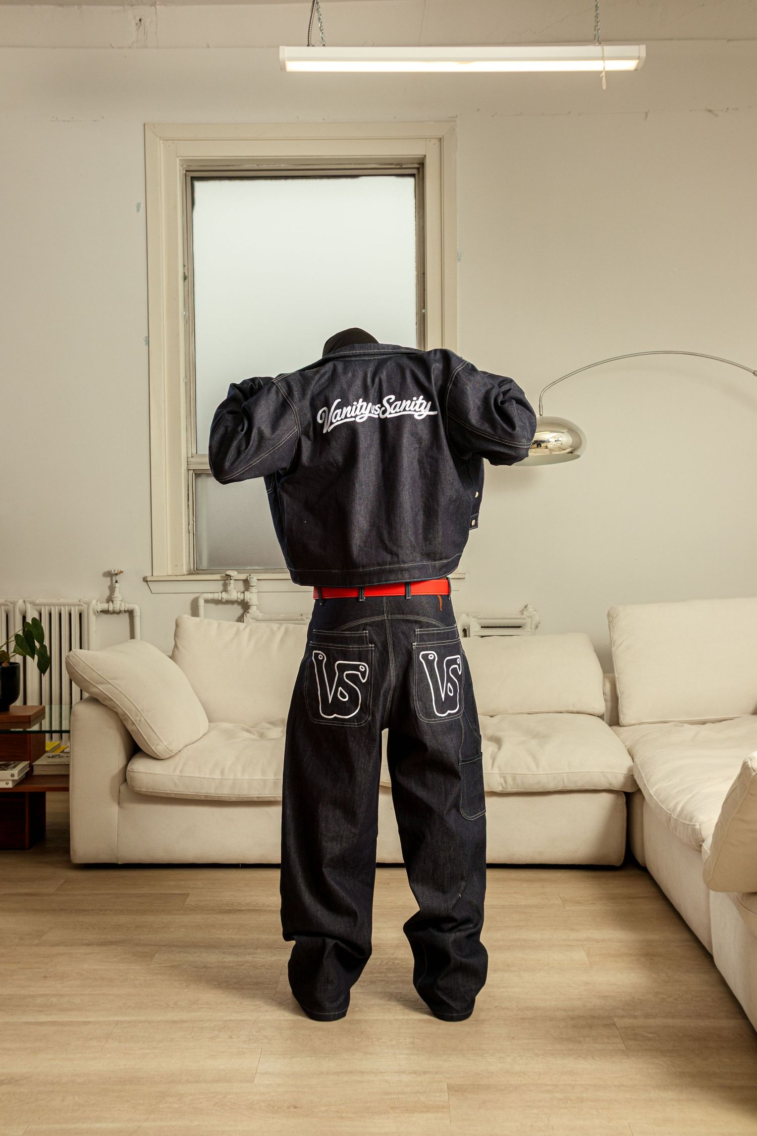 A black racing suit with red accents hangs suspended in a living room with a white sectional sofa in the background.