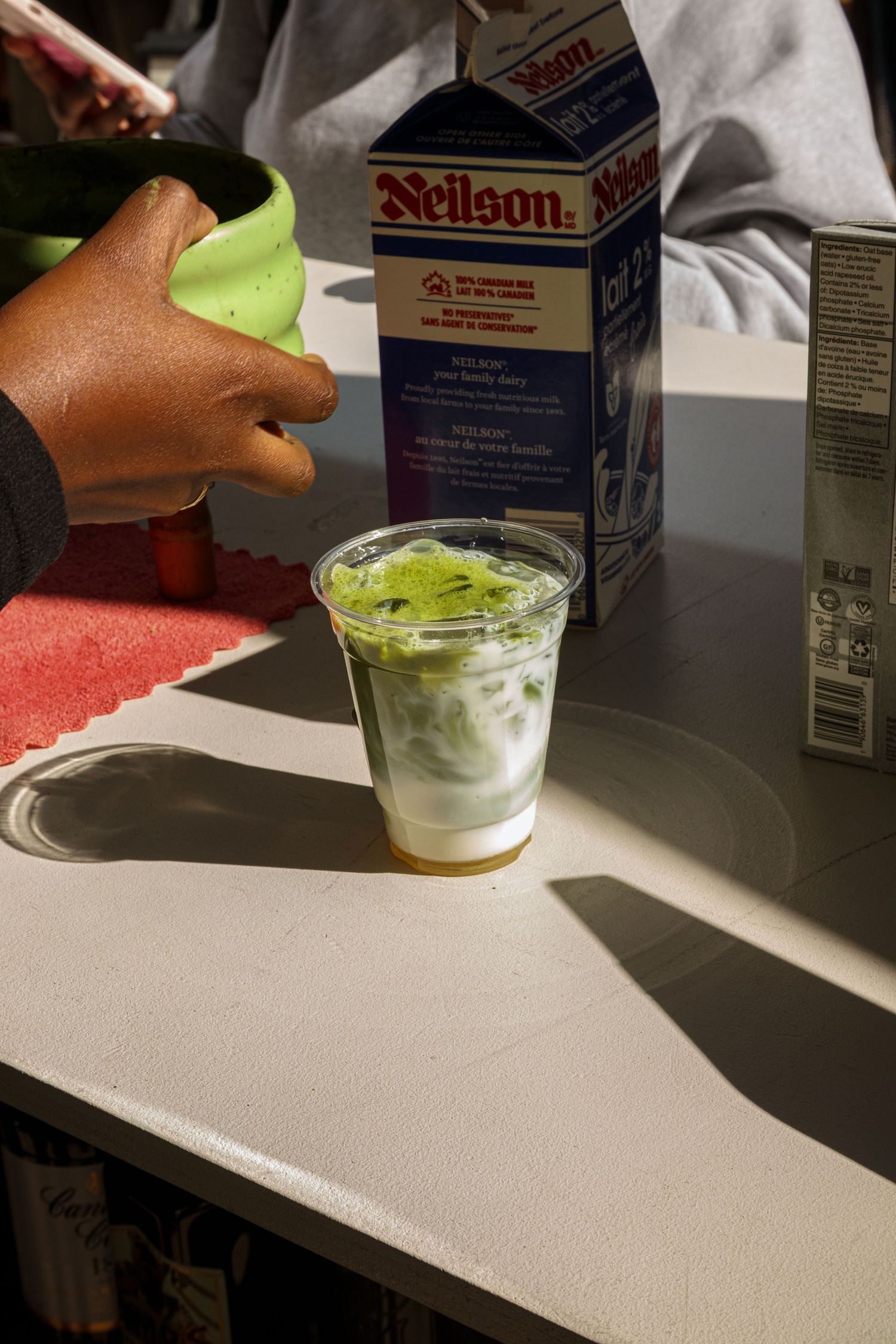 Several glasses of green drinks being prepared on a counter in natural lighting.