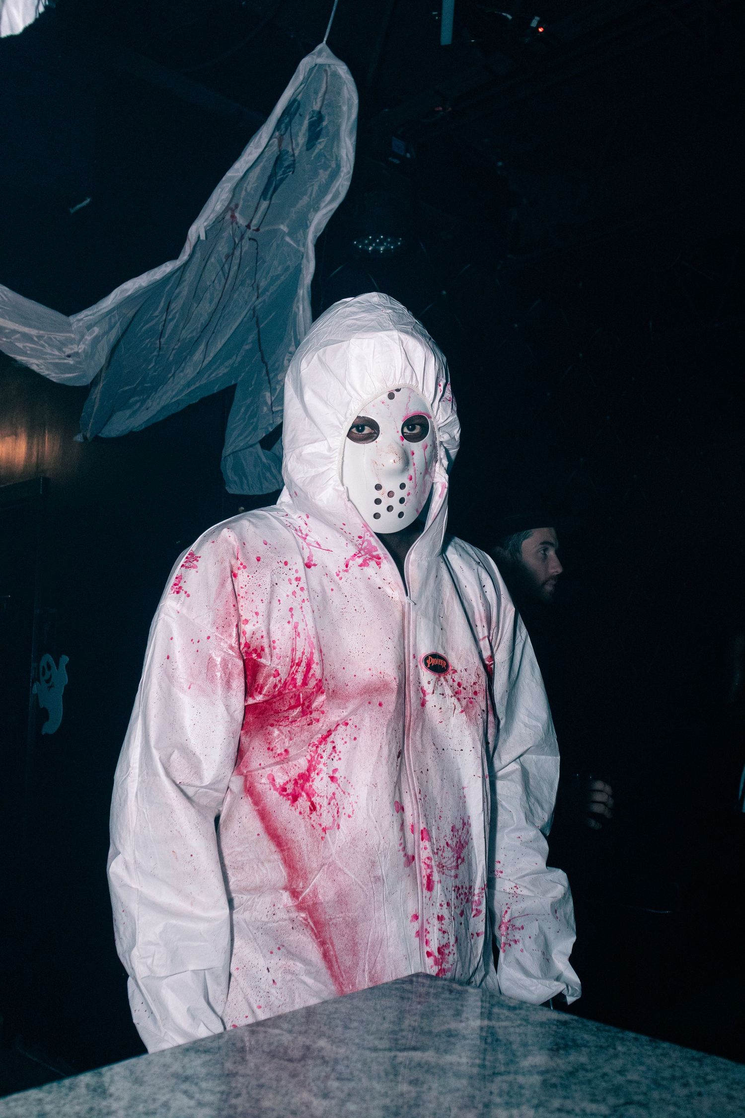 Halloween-themed figure in white protective suit with fake blood splatter in dark setting.