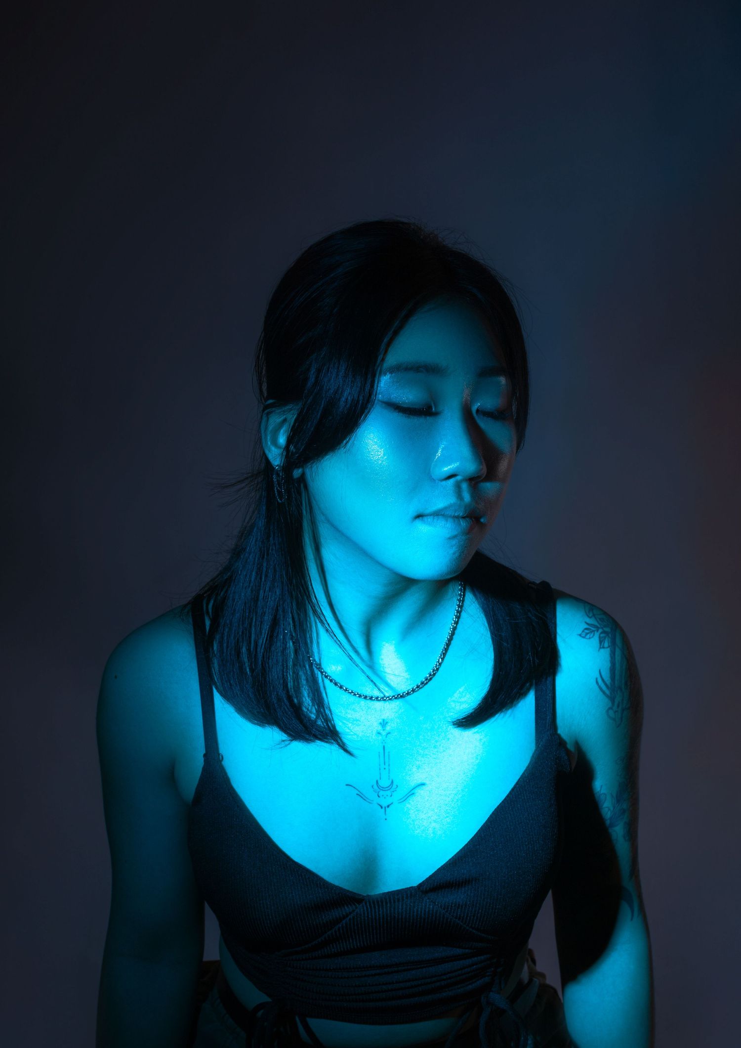 Dramatic blue lighting illuminates a figure in darkness creating a moody atmospheric portrait.