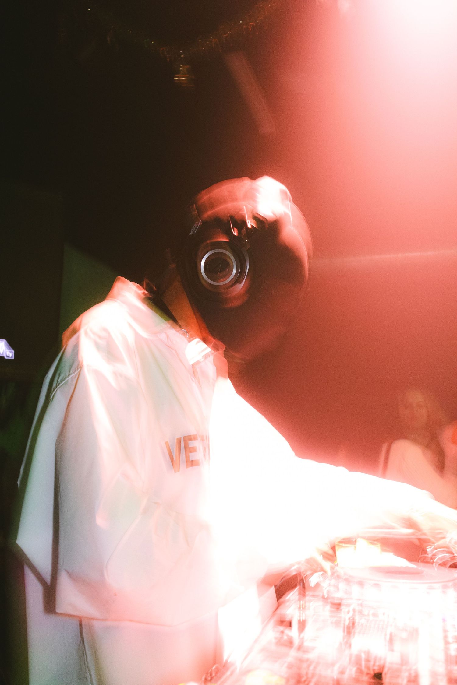 DJ performing in white outfit under red lighting effects.