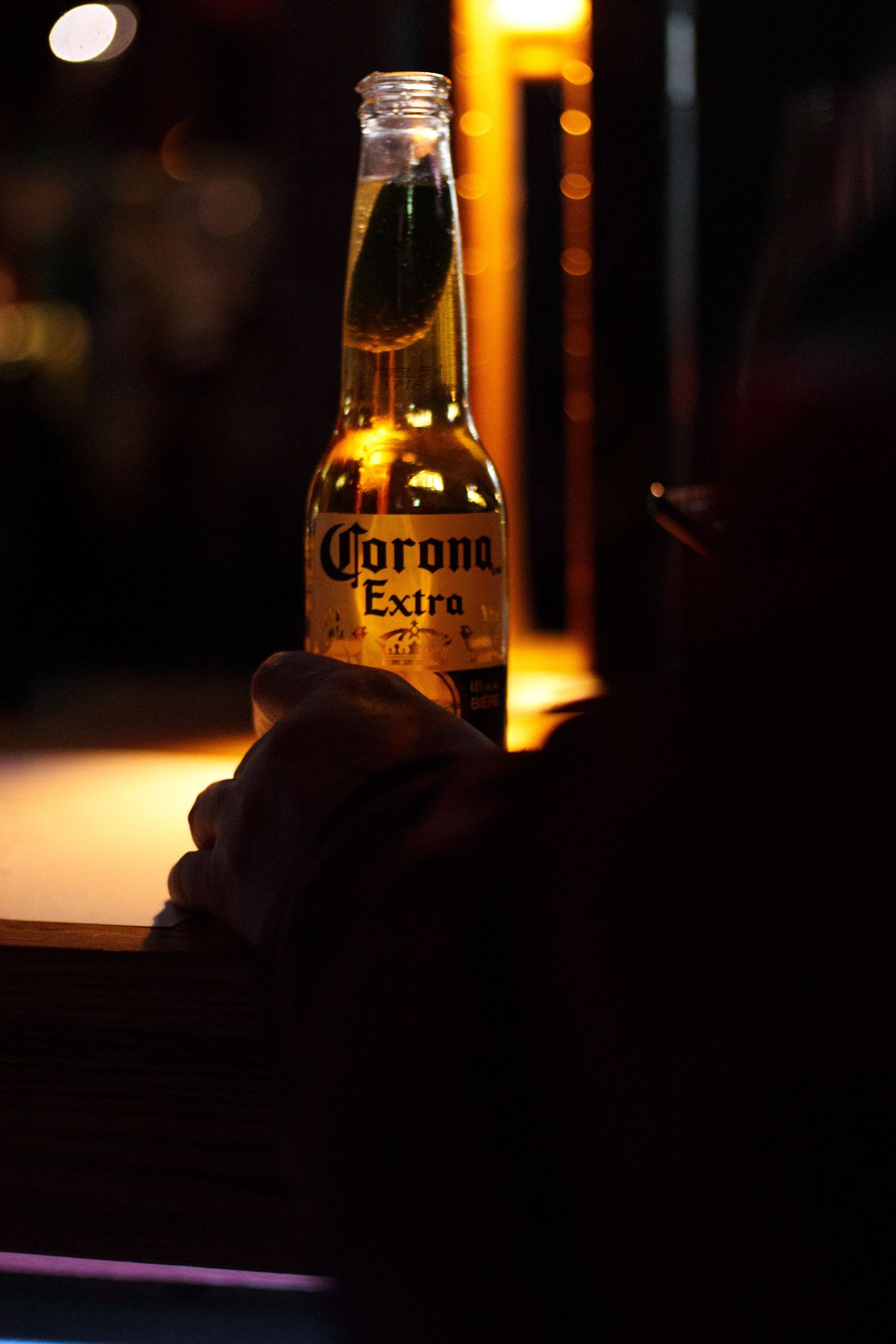 Corona Extra beer bottle glowing in dark ambient bar lighting.