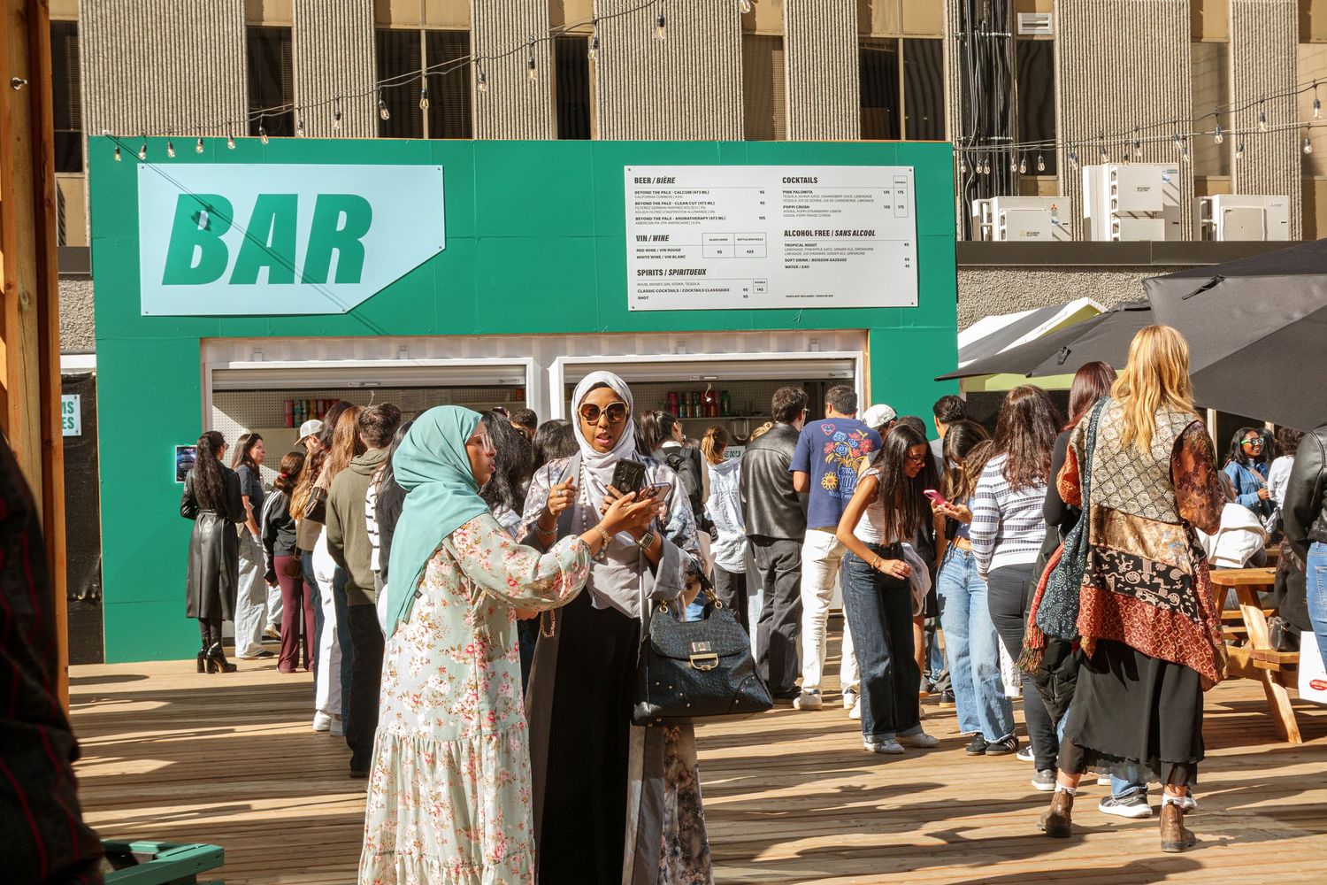 People queuing outside a building with green bar signage visible.