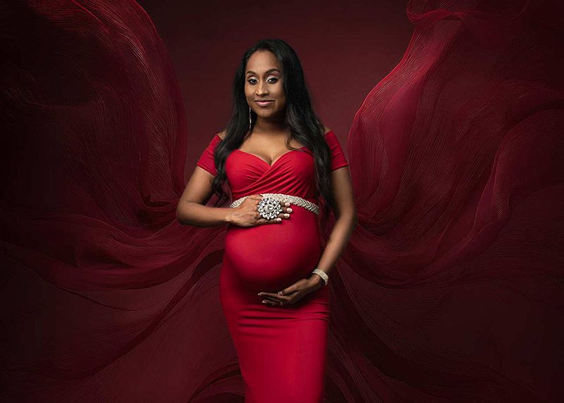 Maternity photographer Spalding - dramatic pregnancy portrait in flowing red maternity gown with dramatic red fabric and dark studio backgro