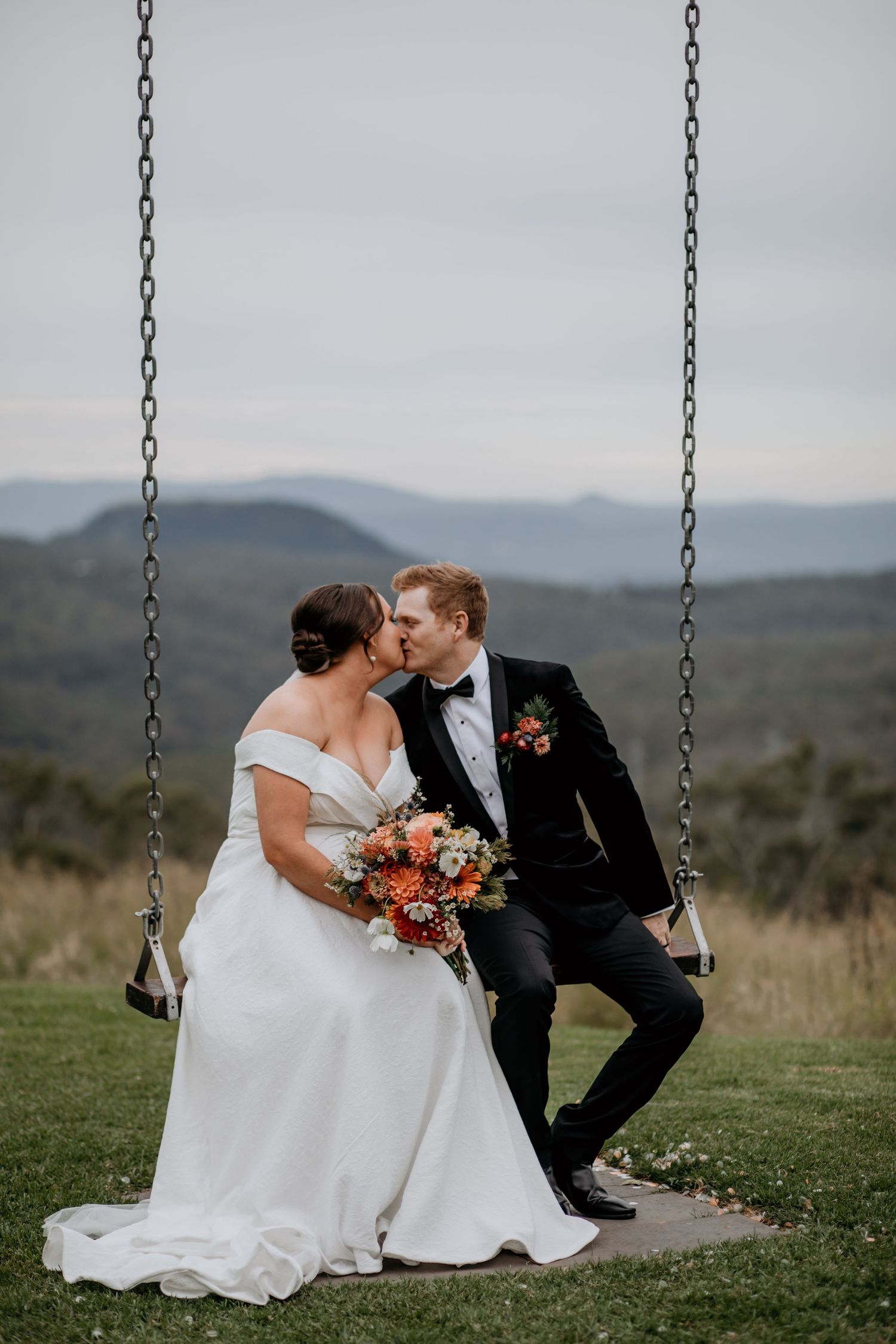 Romantic wedding portrait on a swing with mountain landscape backdrop.