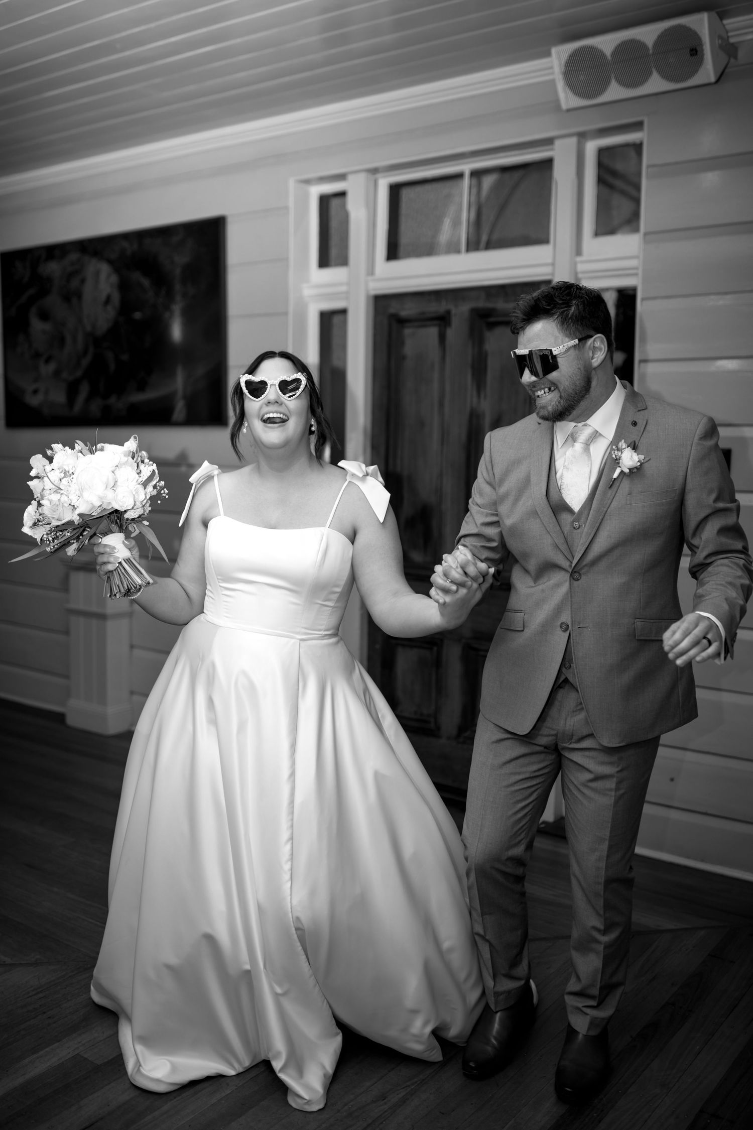 Joyful wedding party wearing sunglasses and dancing outside a white building.