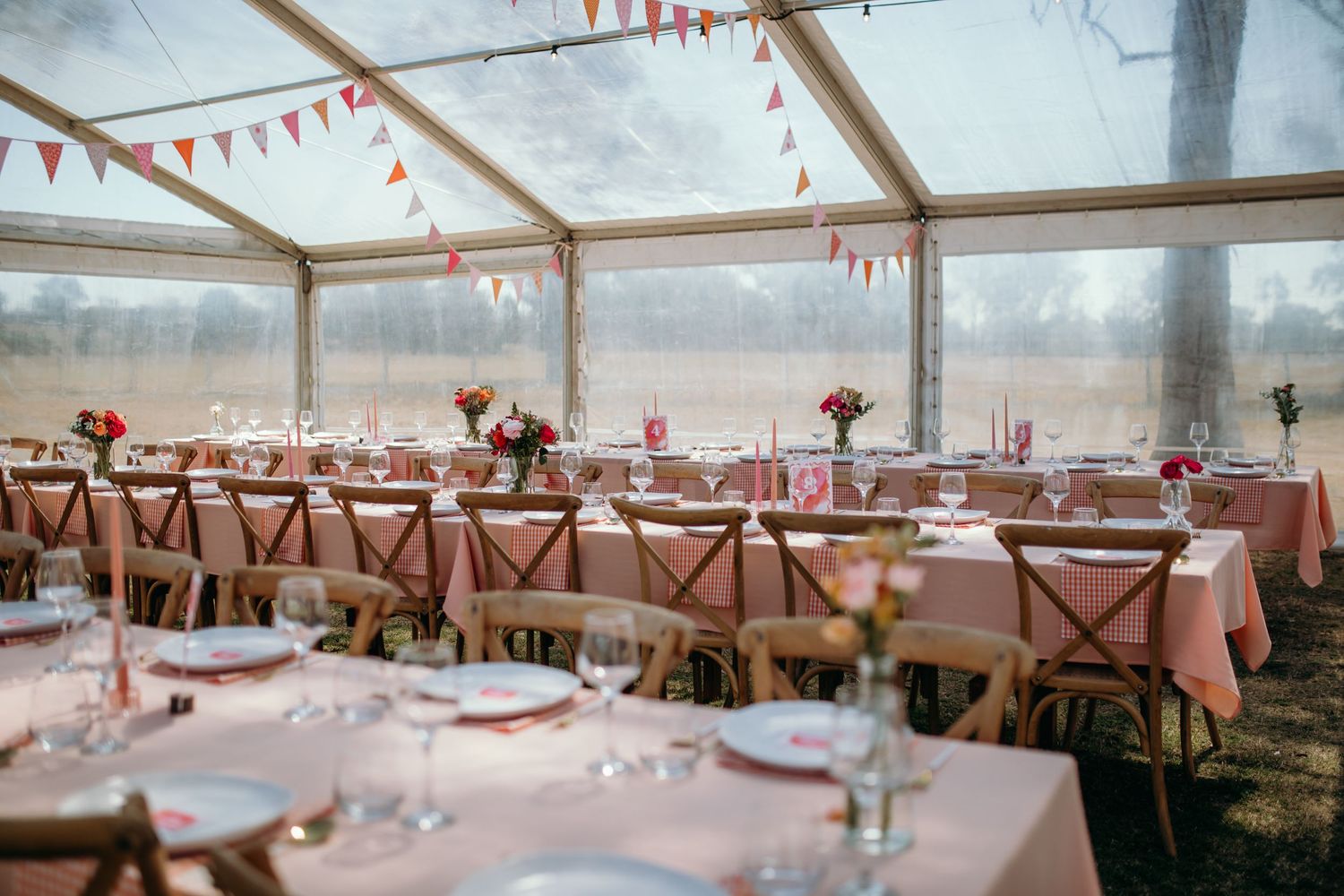 Clear tent reception venue decorated with string lights and coral bunting flags.