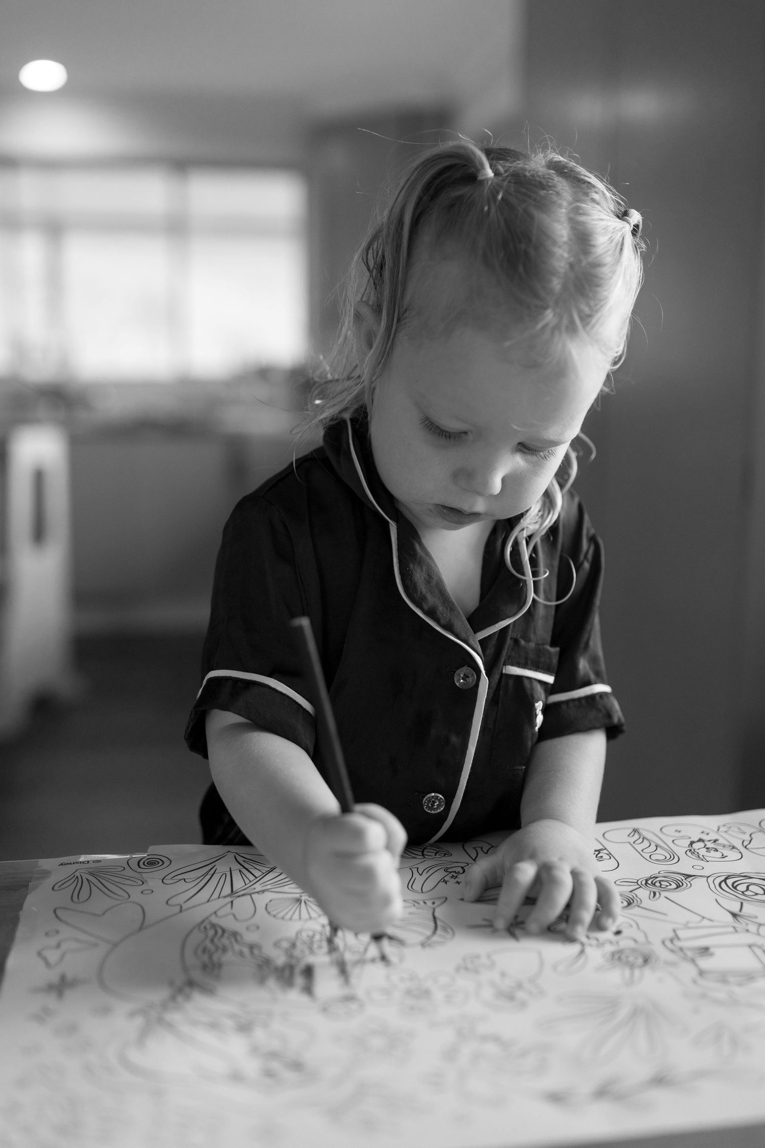 Black and white image of a child drawing intently at a table.