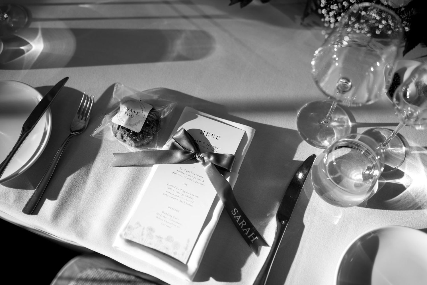 Wedding reception place settings with menus and glassware in natural light.