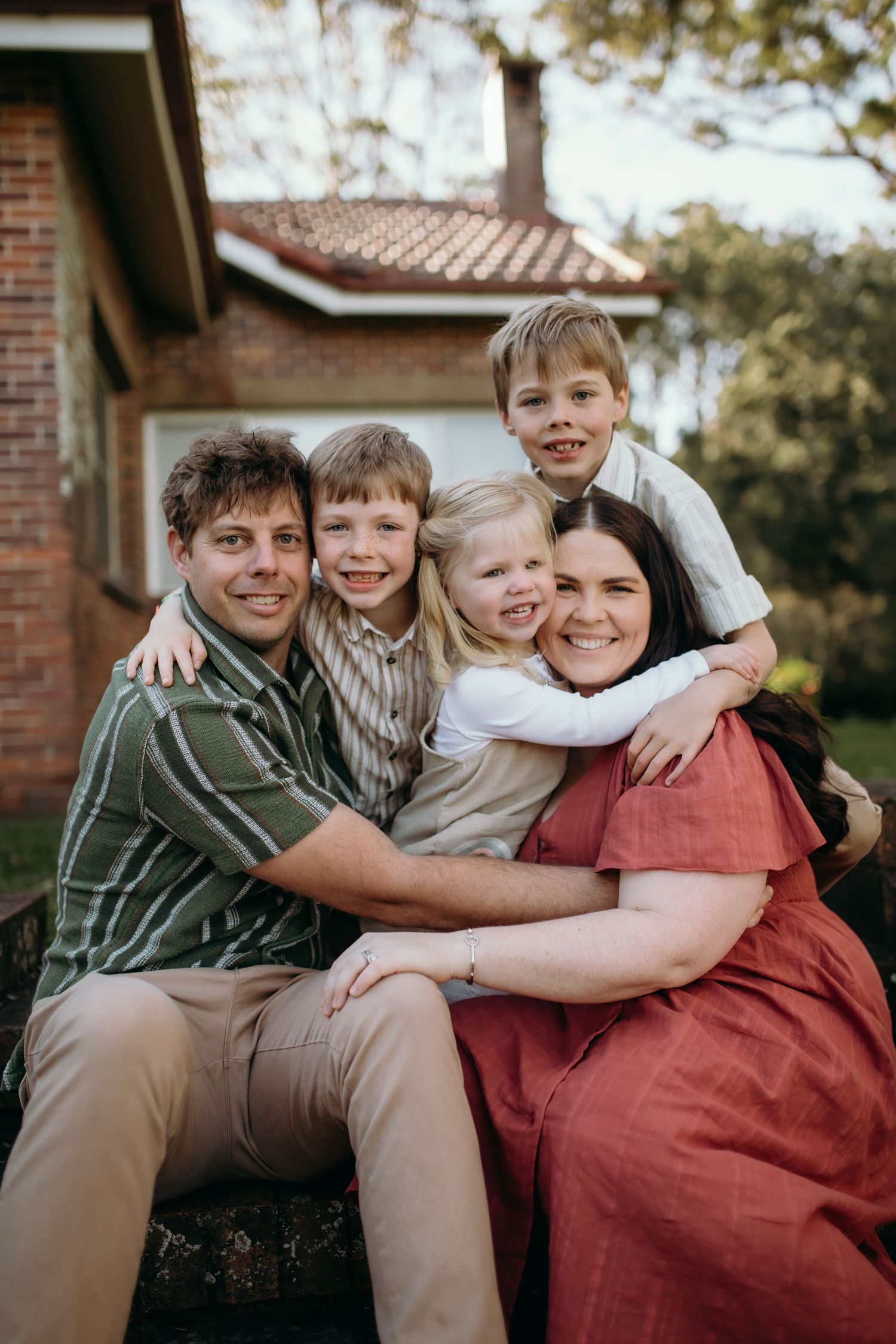 Family portrait with children cuddling together outdoors in casual clothing.