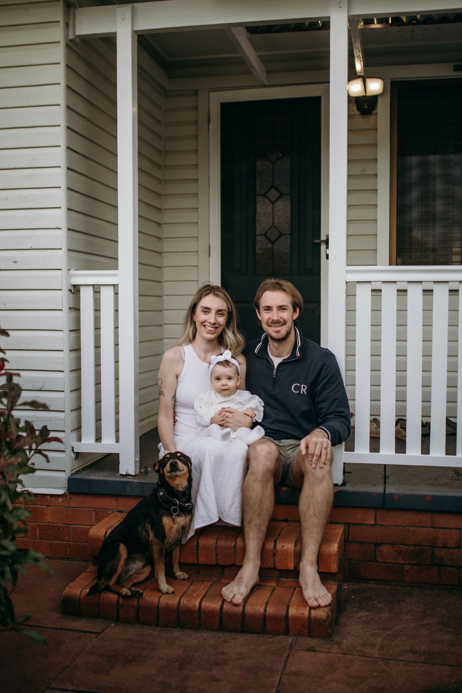 Family sitting together on front porch steps of white house with their dog.