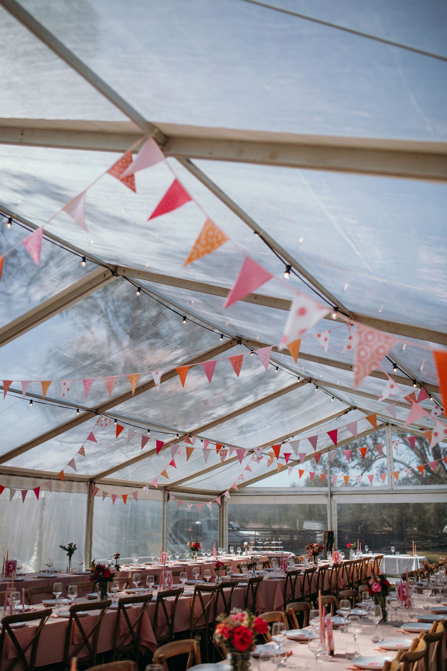 Wedding reception tent with coral bunting flags and wooden cross-back chairs.