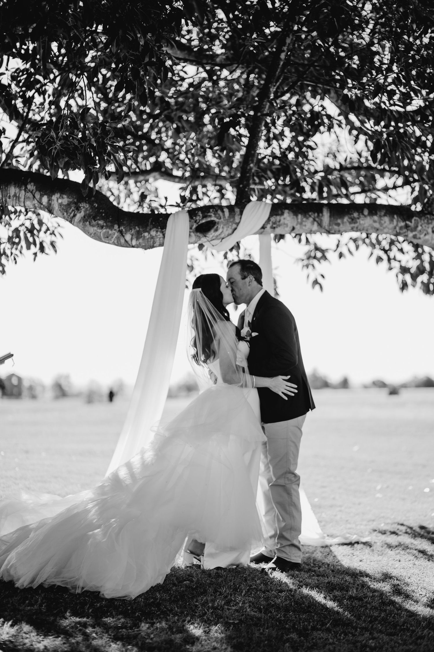 Black and white wedding photos under a tree showing flowing white dress movement.